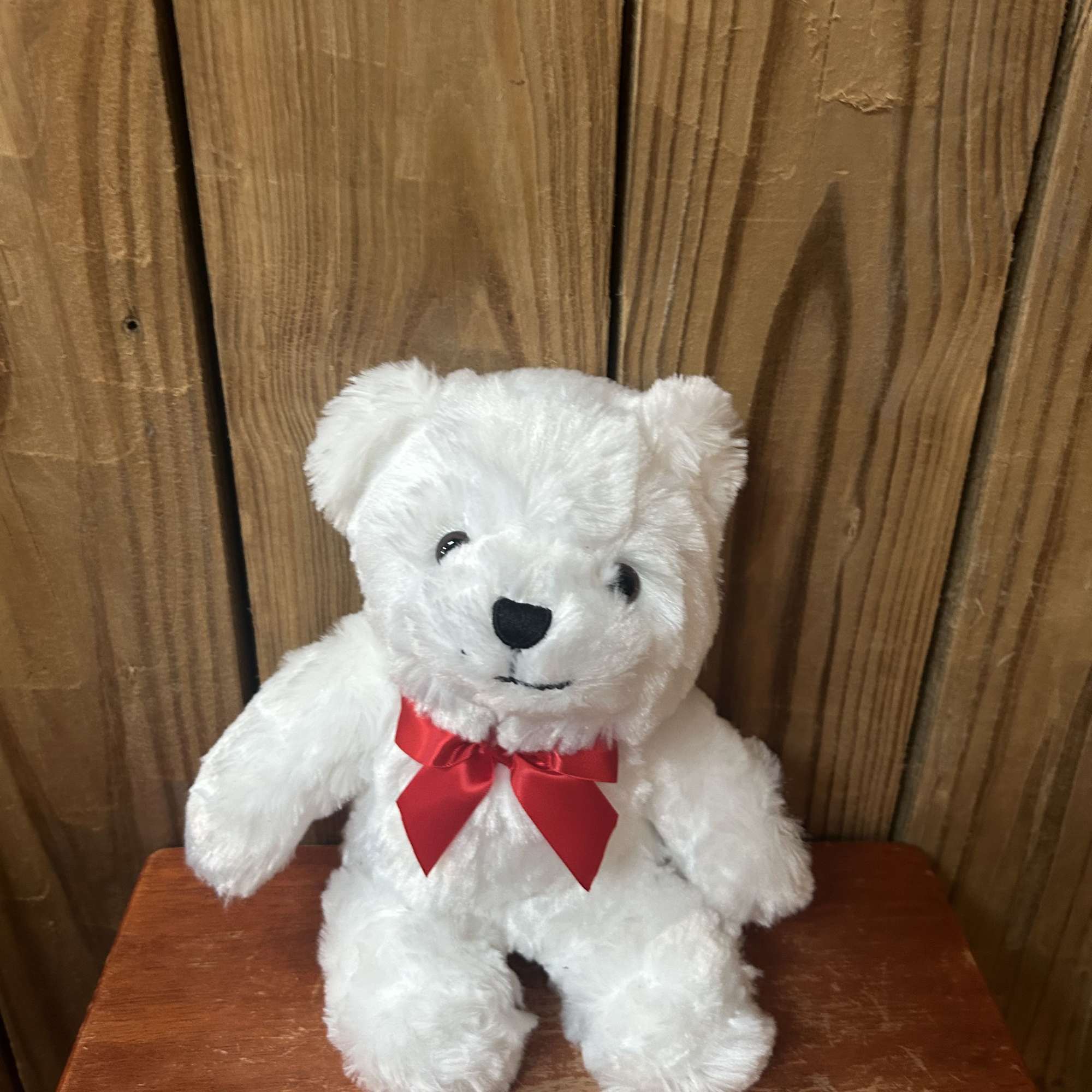 Small white teddy bear with a red bow sitting on a wooden surface.