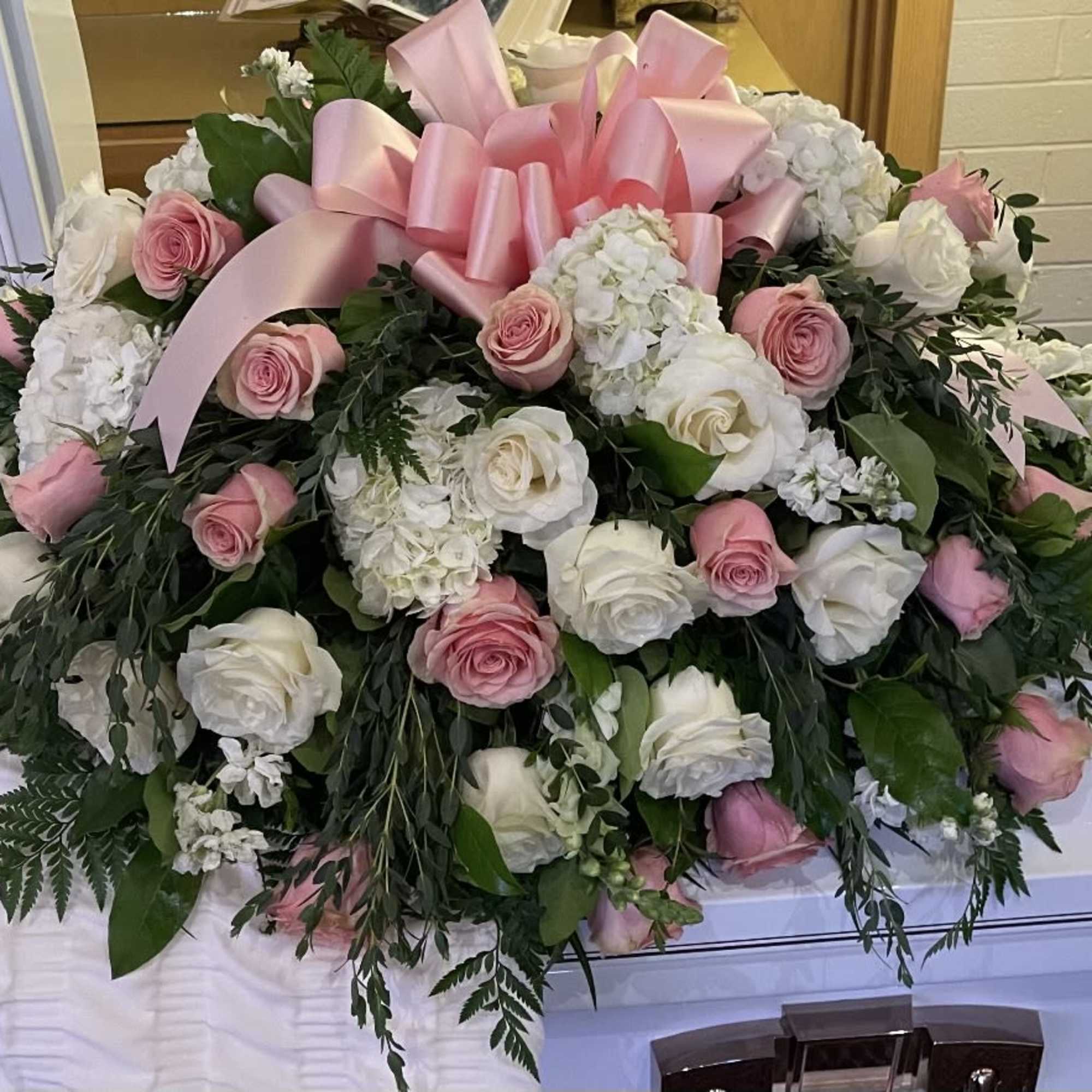 Large pink and white rose arrangement with a pink ribbon on a casket