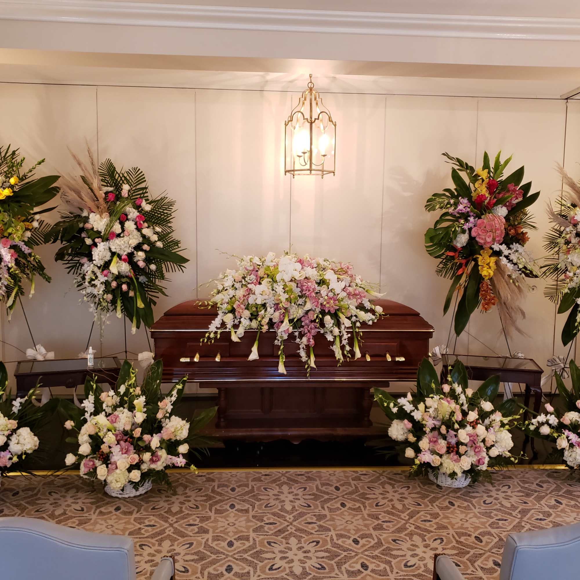 Funeral casket surrounded by large floral sprays and arrangements
