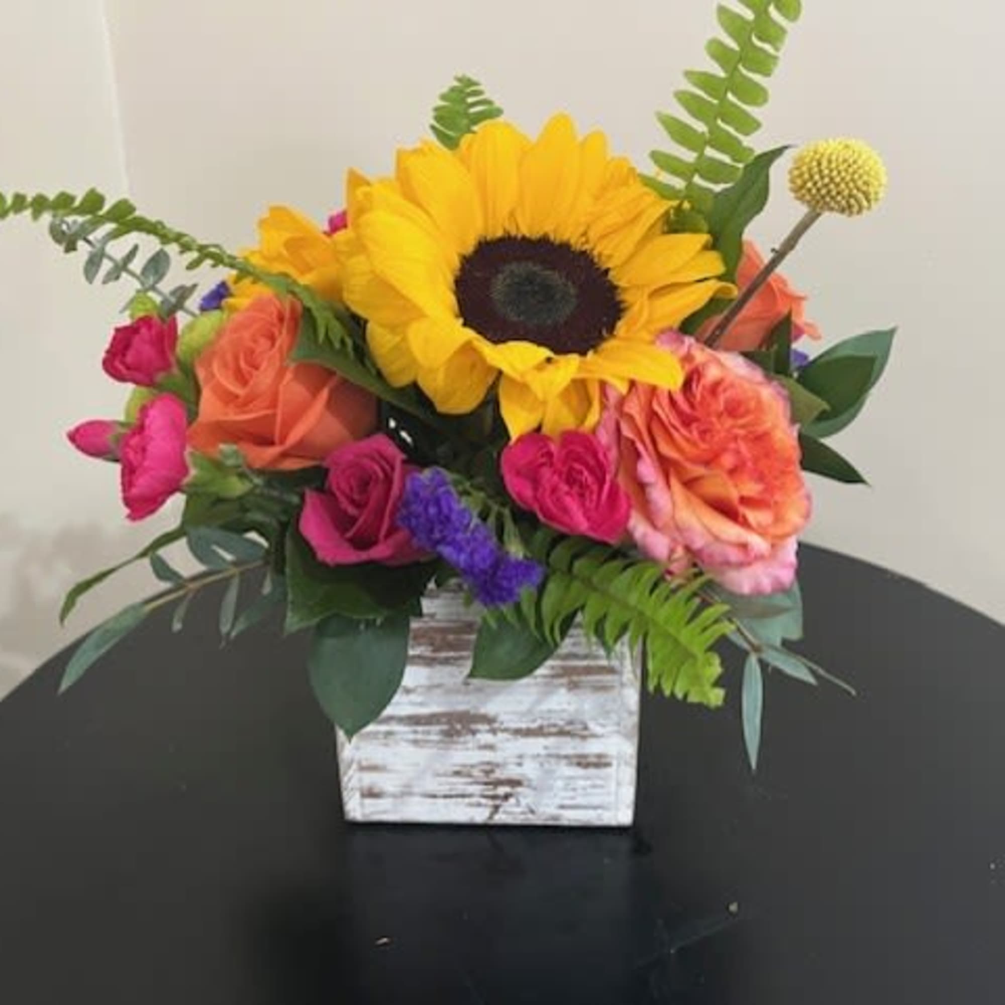 Bright sunflower and mixed roses in a whitewashed wooden cube vase