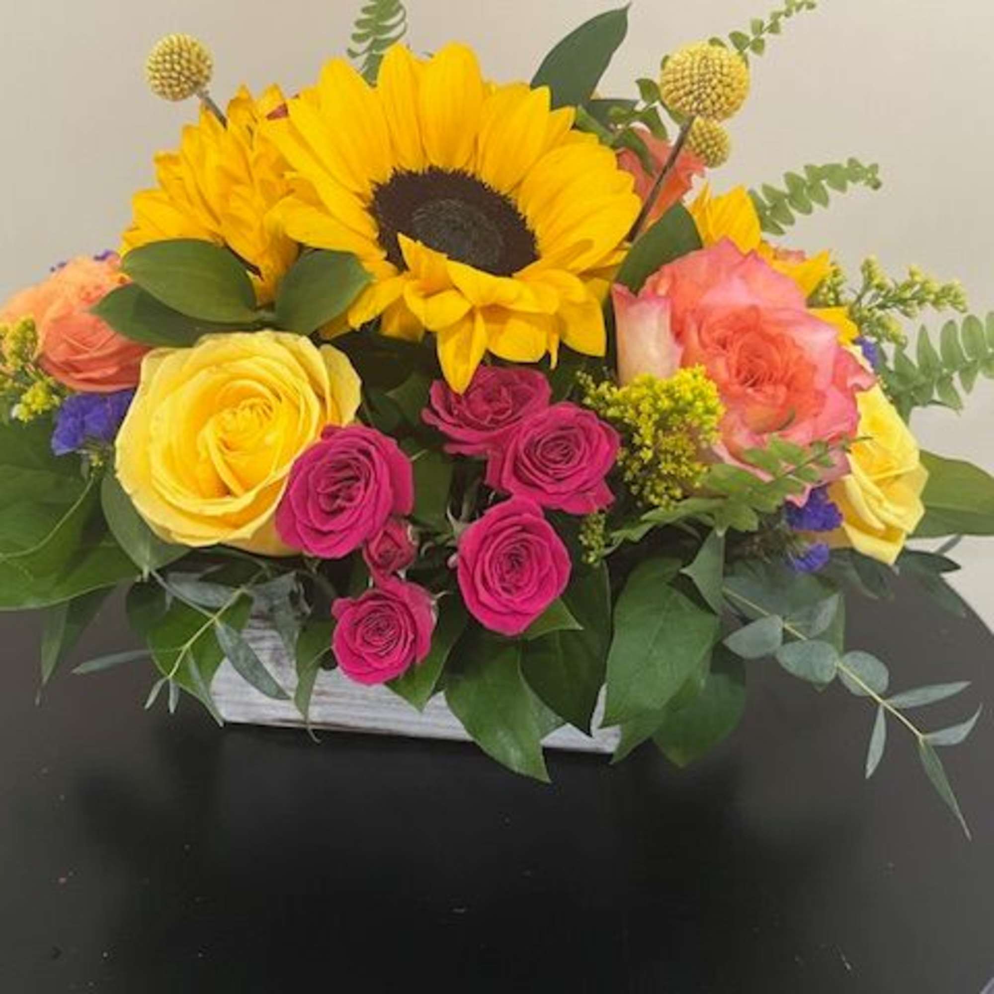 Bright arrangement of sunflowers and mixed roses in a white rectangular container