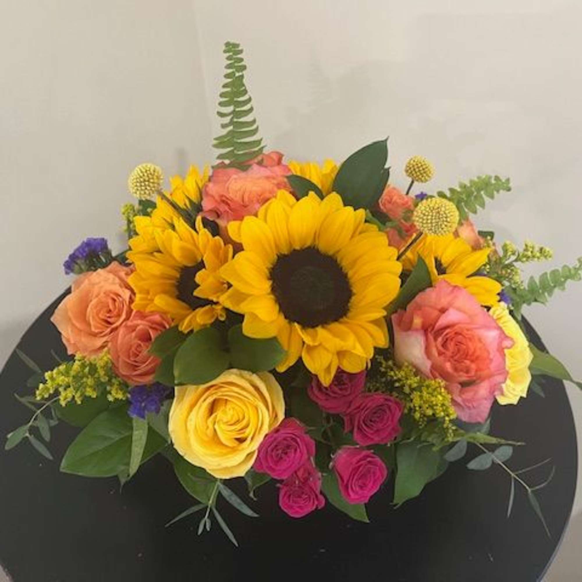 Low arrangement of bright sunflowers and multicolored roses on a black round surface