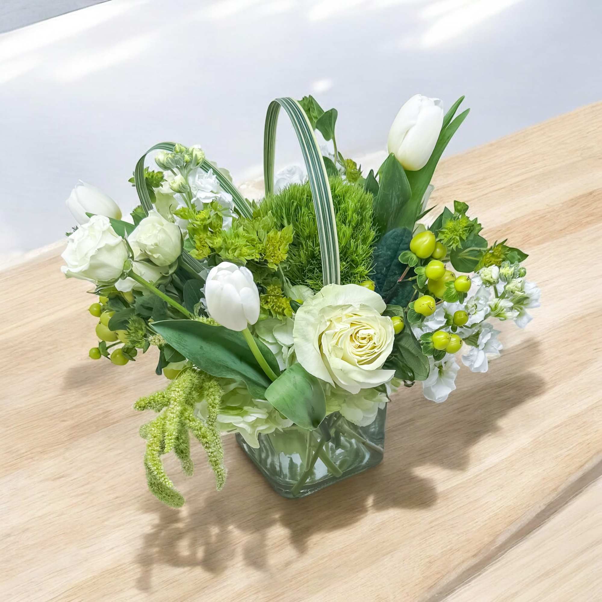 White flowers and tulips arranged in a square glass vase