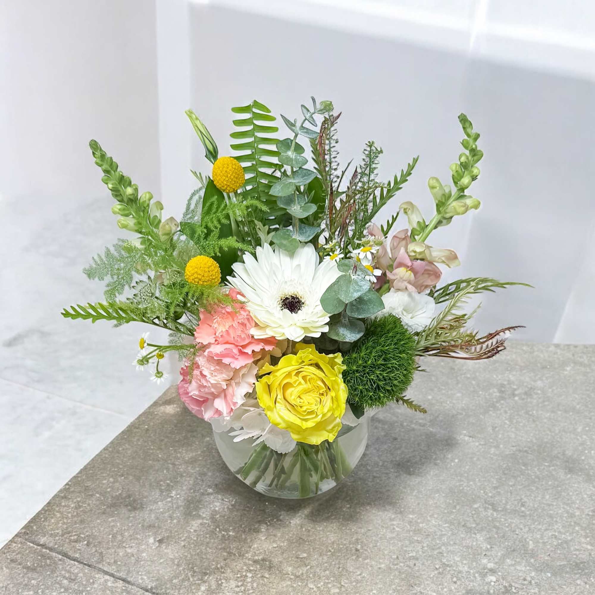 Mixed bouquet in a clear glass vase with white, yellow, and pink blooms