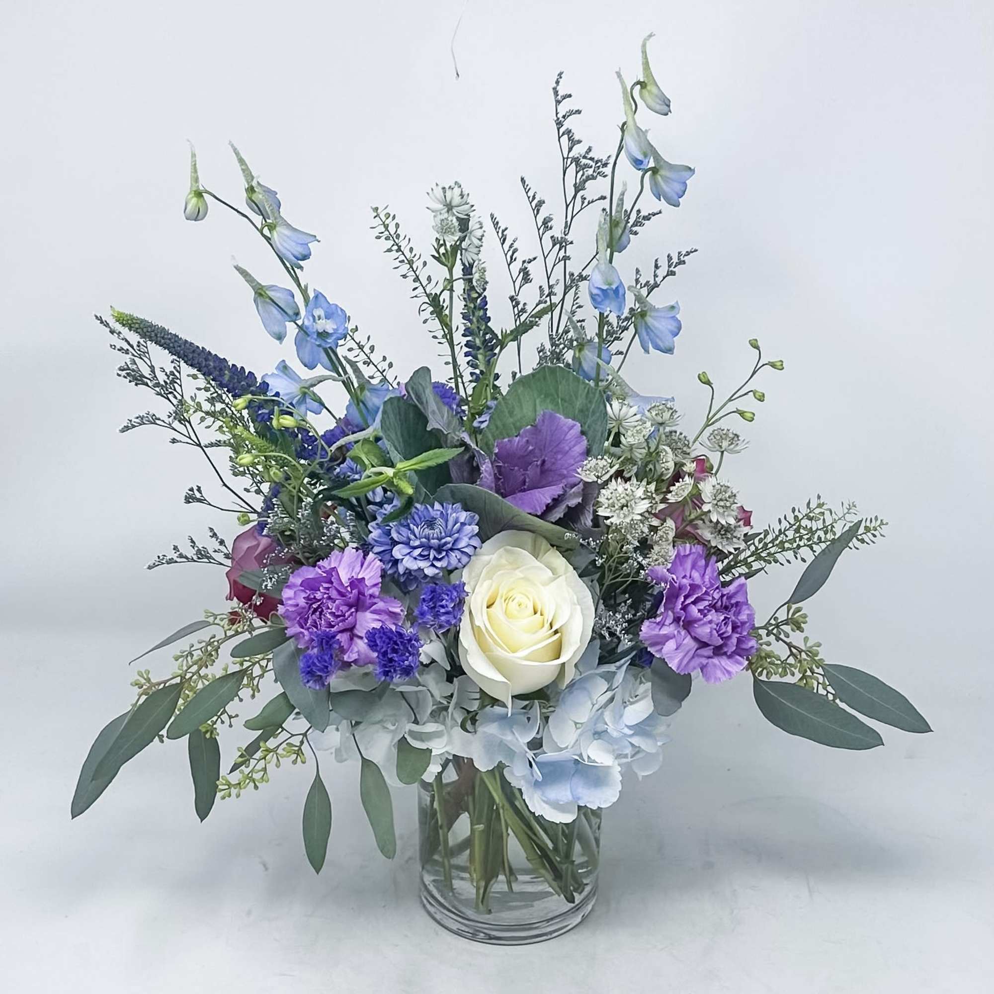 Mixed bouquet in a clear glass vase with blue, purple, and white flowers