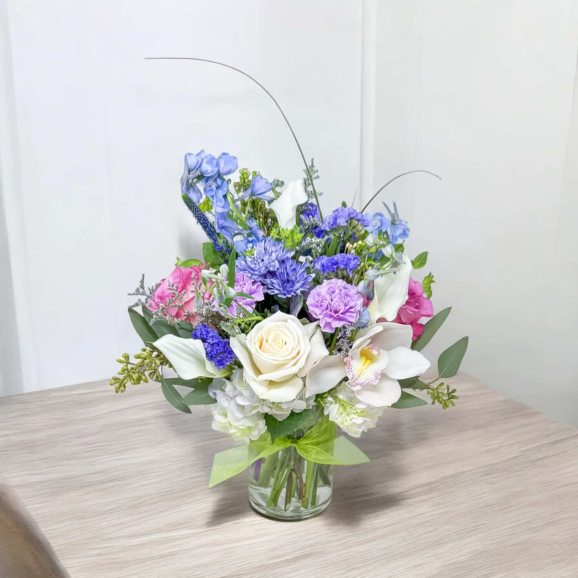 Mixed bouquet of blue, purple, pink, and white flowers in a glass vase