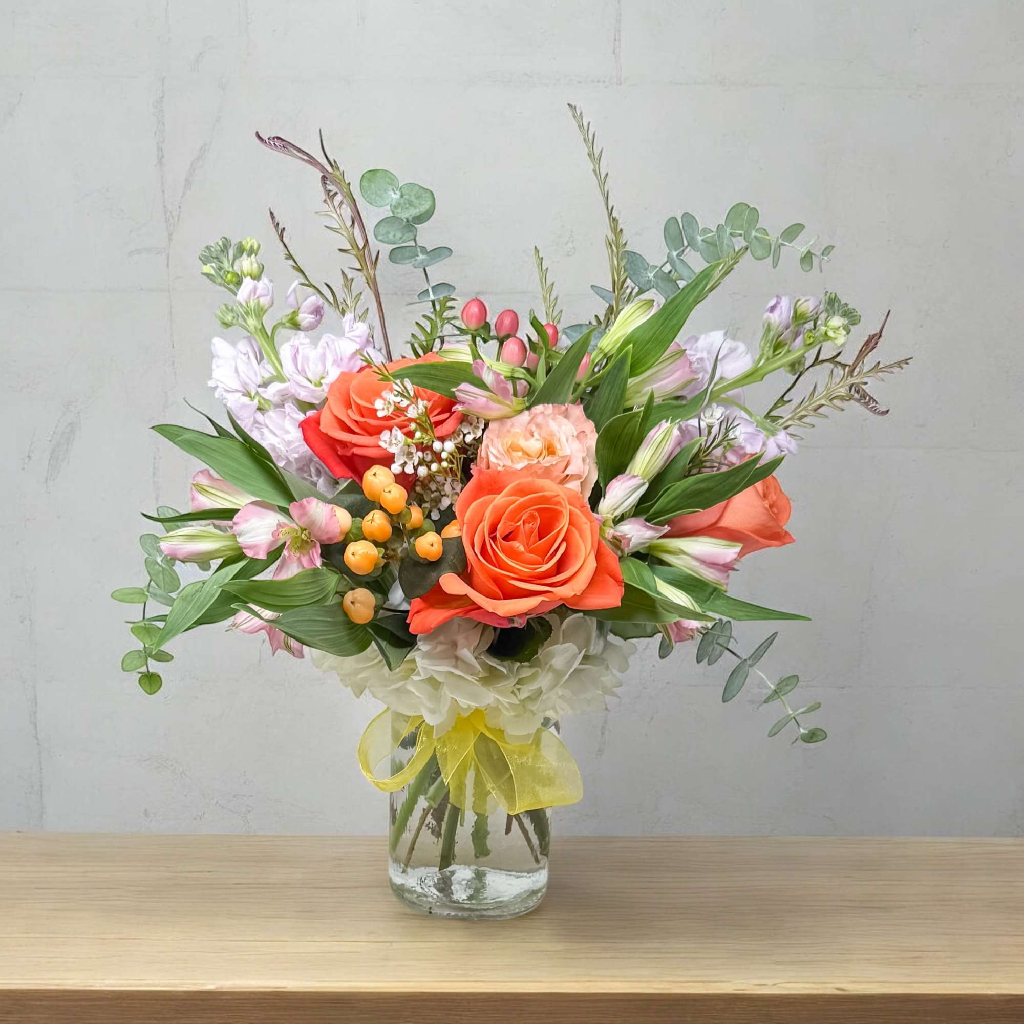 Bouquet of orange roses and pastel flowers in a glass vase with a yellow ribbon