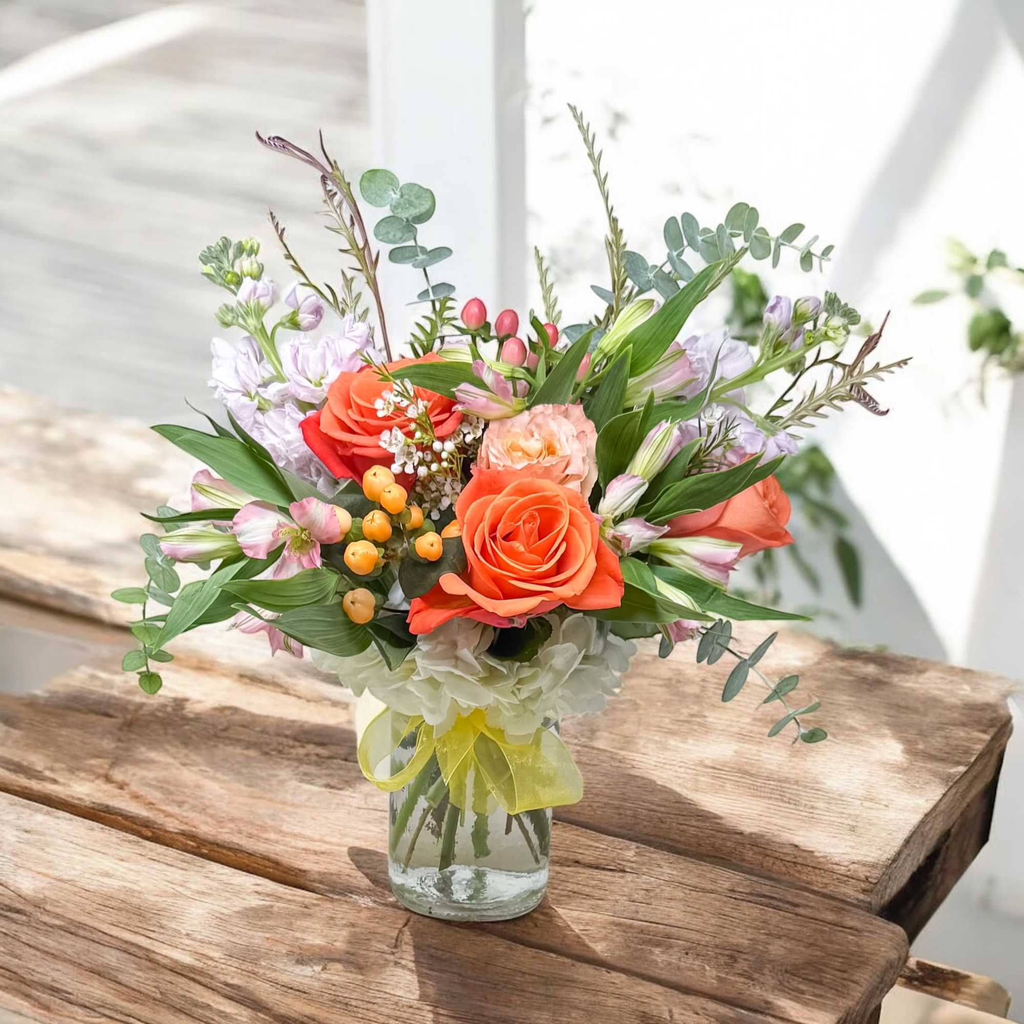 Mixed bouquet of orange roses and pastel flowers in a glass vase