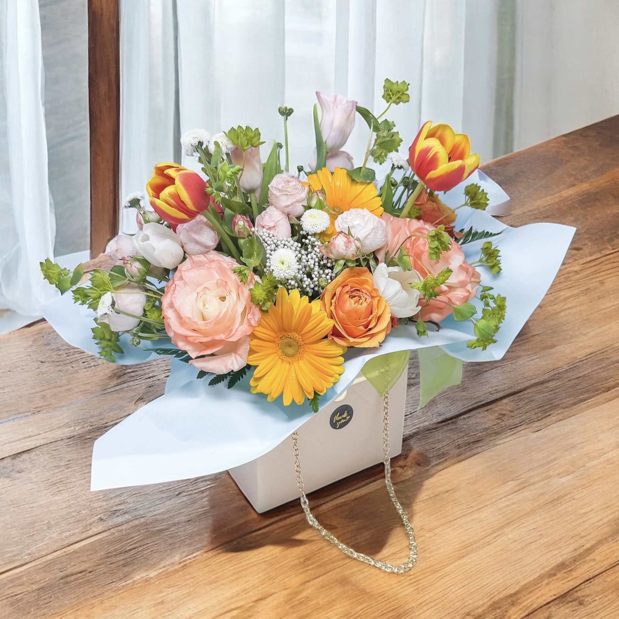 Mixed bouquet of pink, orange, and yellow flowers in a gift box