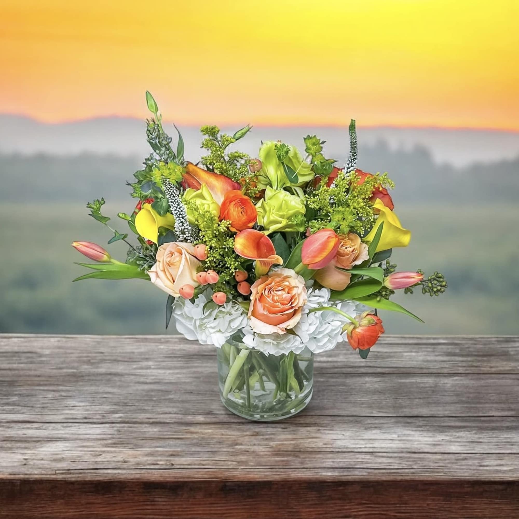 Mixed bouquet of orange, yellow, and white flowers in a glass vase