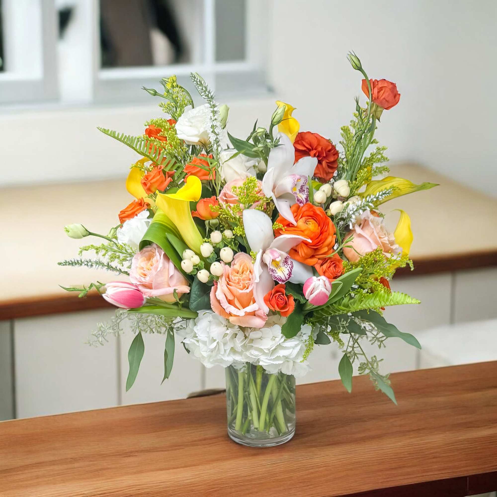 Mixed bouquet of orange, yellow, pink, and white flowers in a glass vase