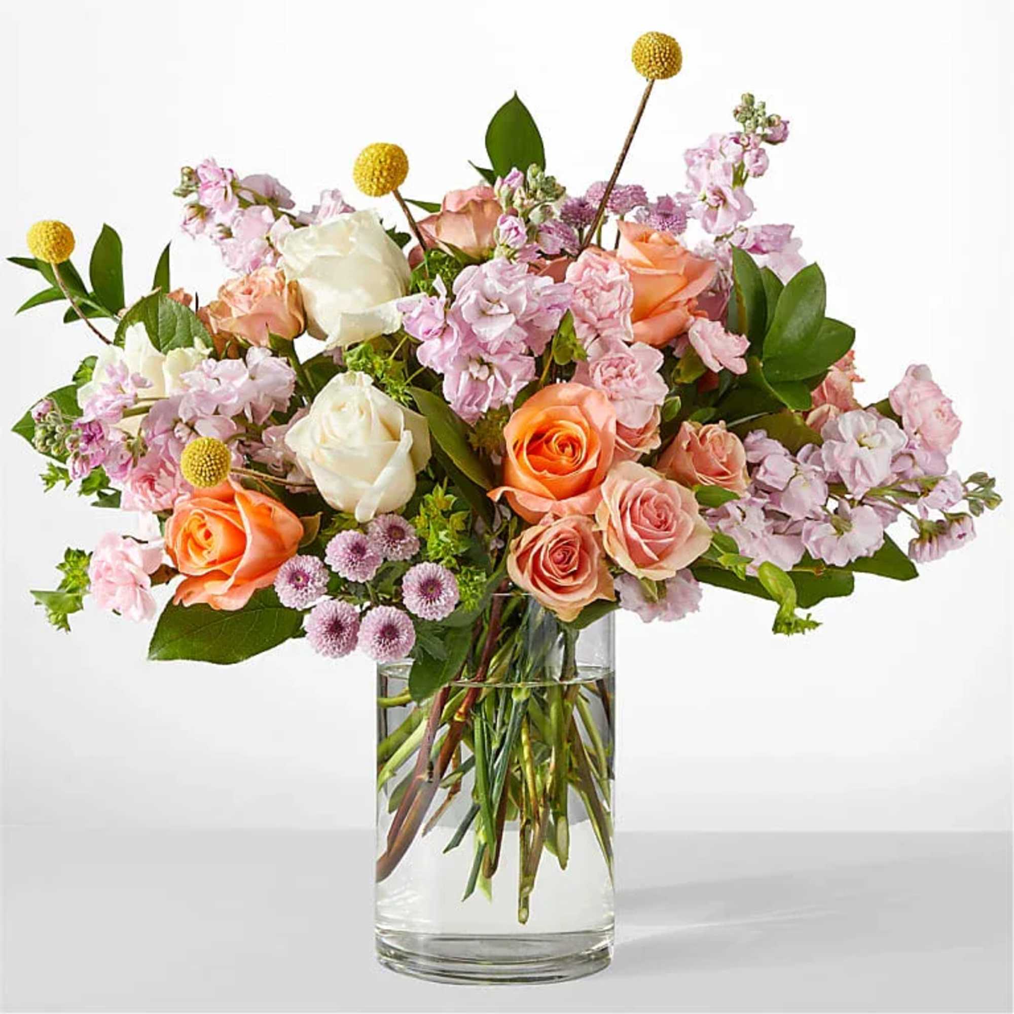 Peach and white rose arrangement with pink stock and yellow accents in a clear glass cylinder vase