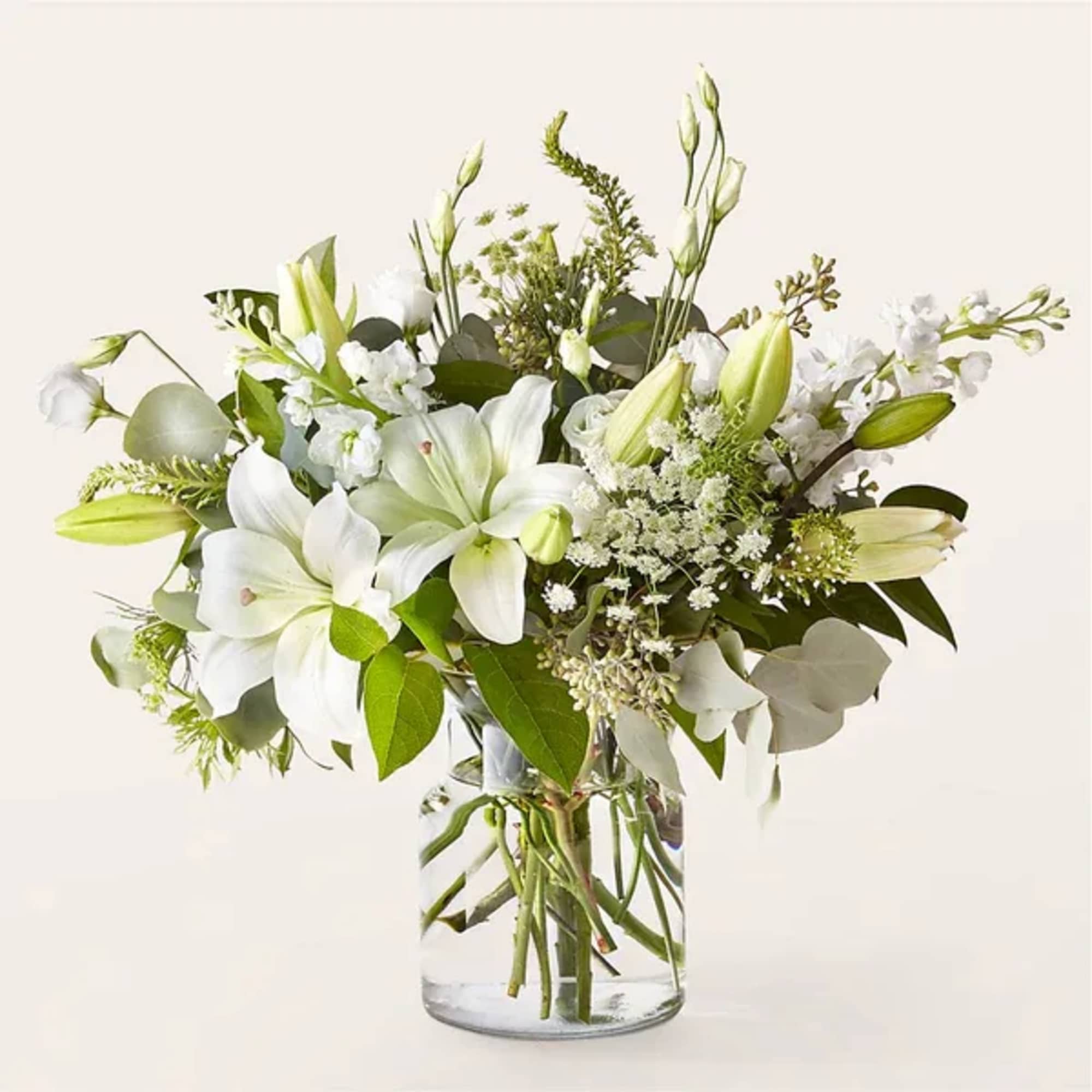 White lilies and mixed white flowers arranged in a clear glass cylinder vase.