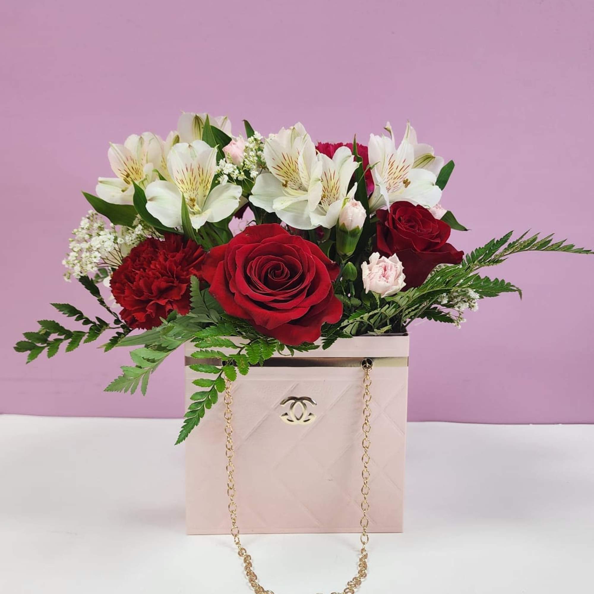 Red roses and white lilies in a pink gift box with a gold chain