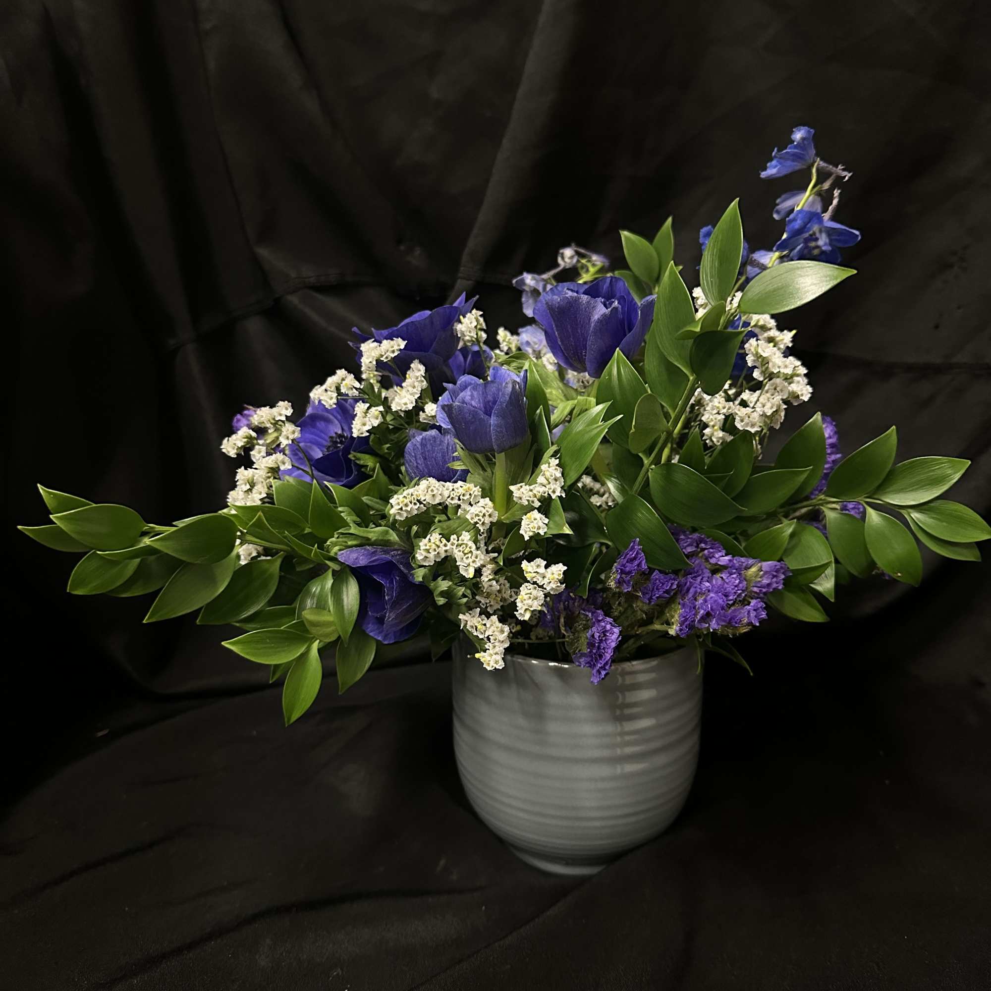 Blue and purple anemones with white fillers and glossy greens in a