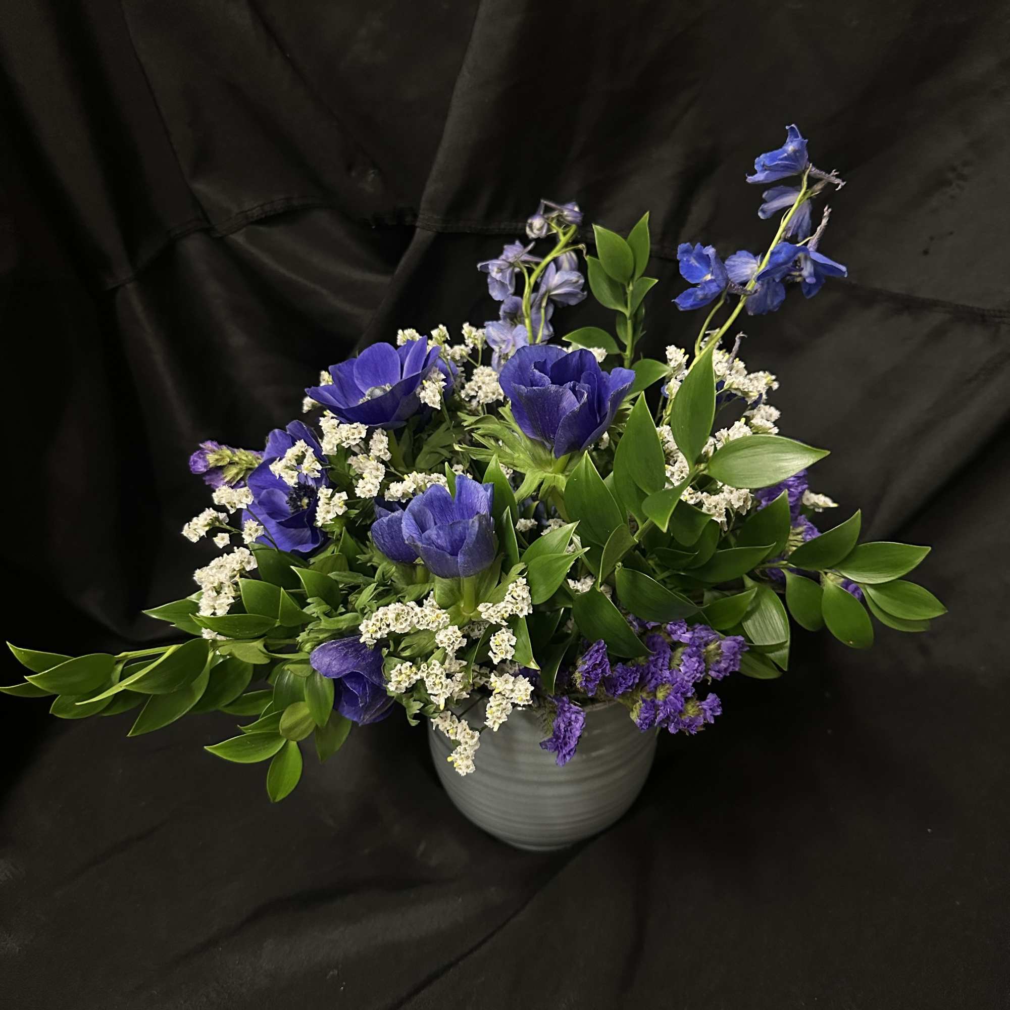 Blue and purple anemones with white fillers and glossy greens in a