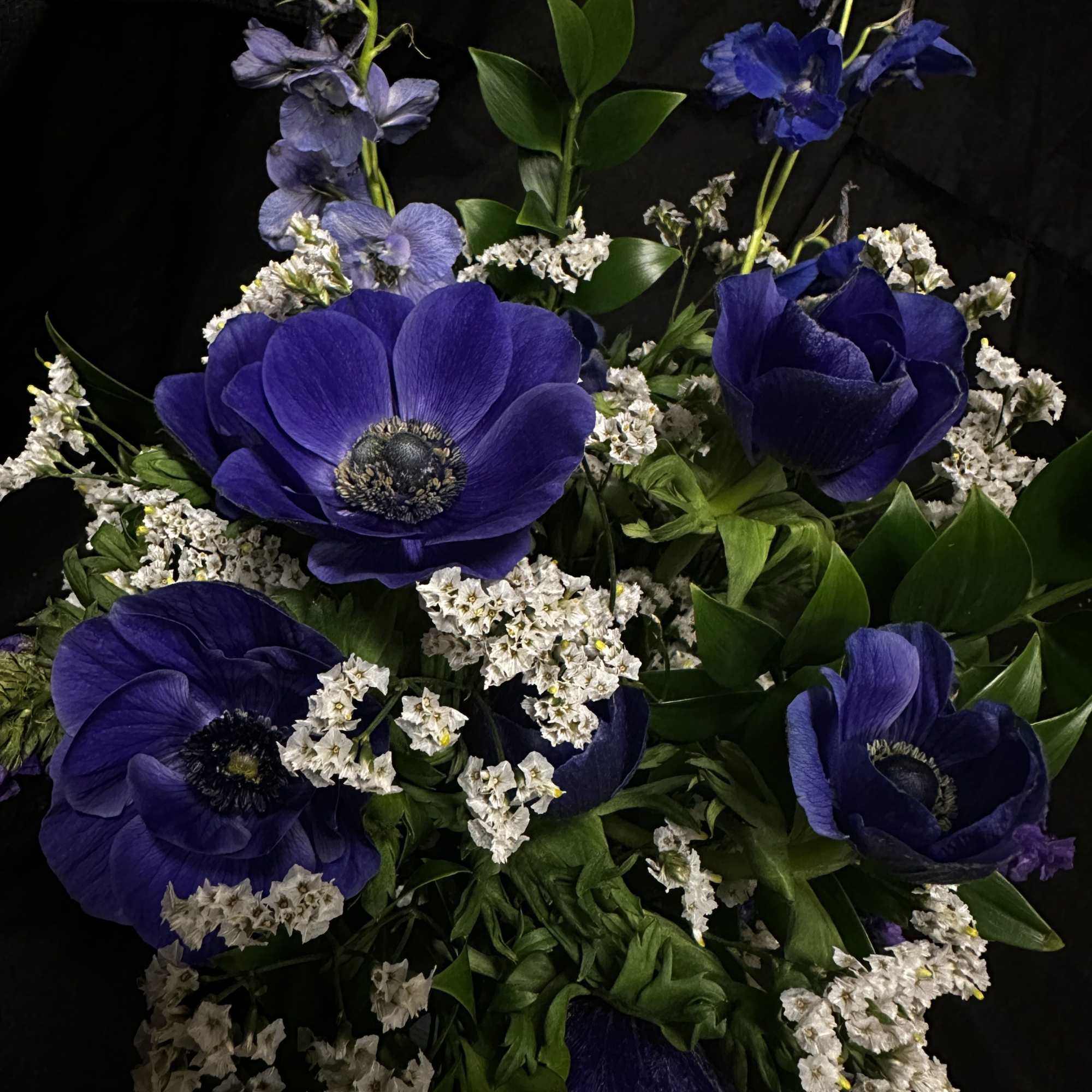 Blue and purple anemones with white fillers and glossy greens in a
