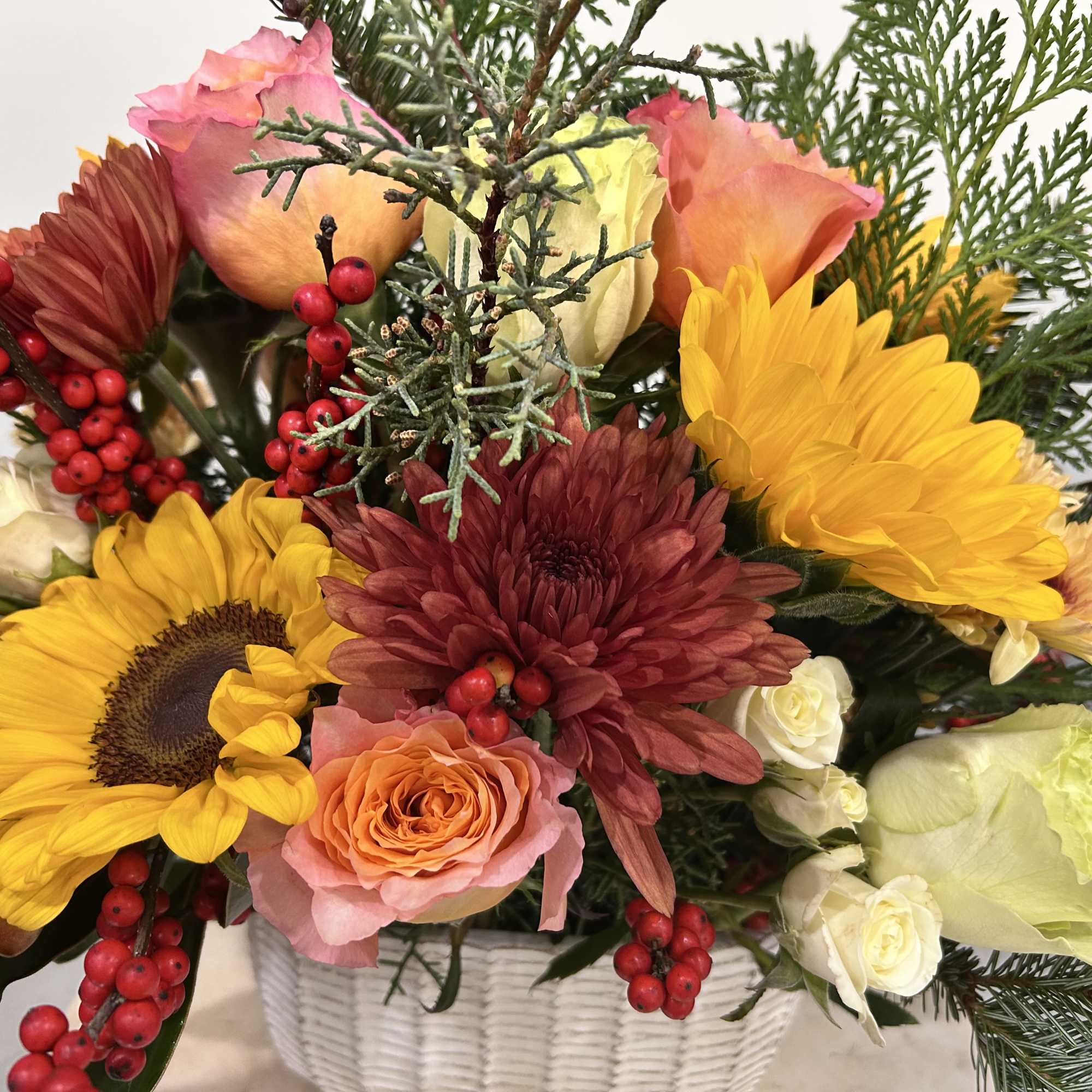 Basket arrangement with sunflowers, roses, and red berries