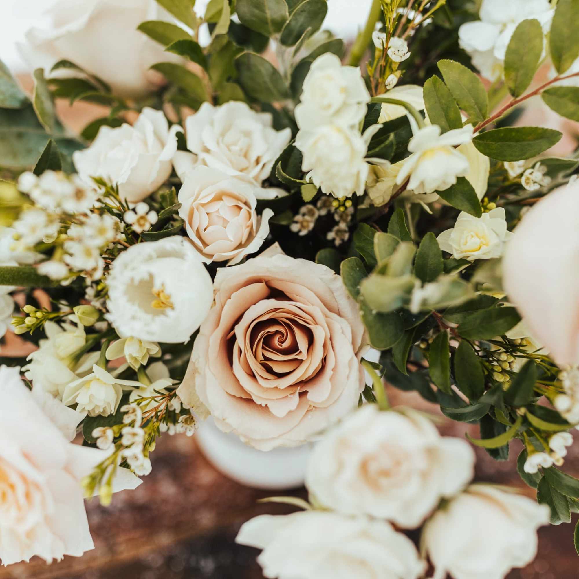 Arrangement of blush roses and white flowers in a white vase on a wooden surface