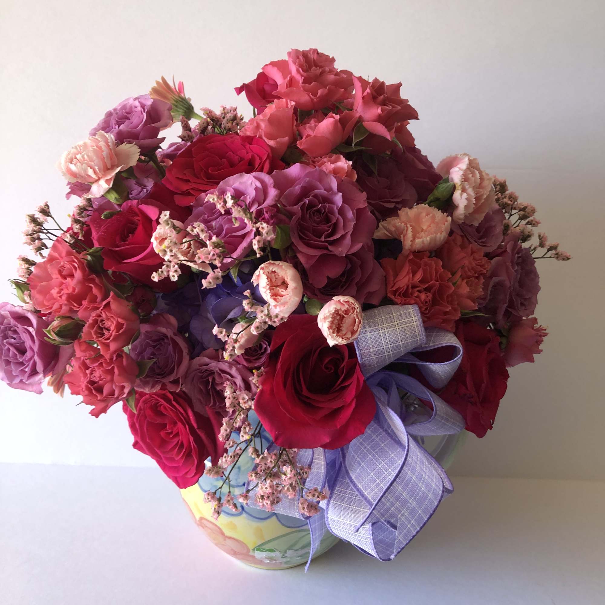 Bouquet of pink and purple roses in a decorative vase with a lavender ribbon