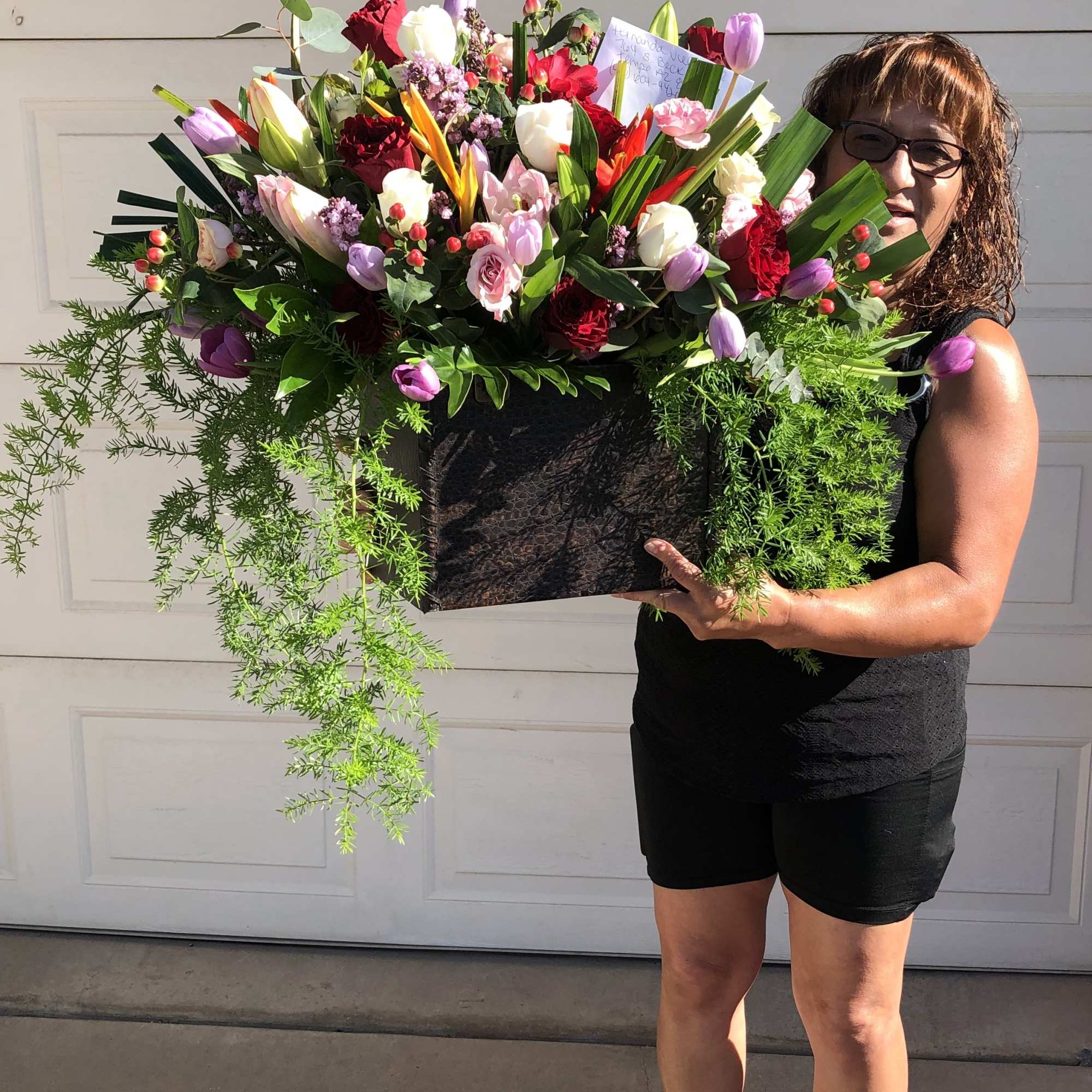 Large mixed flower arrangement in a black container held by a woman