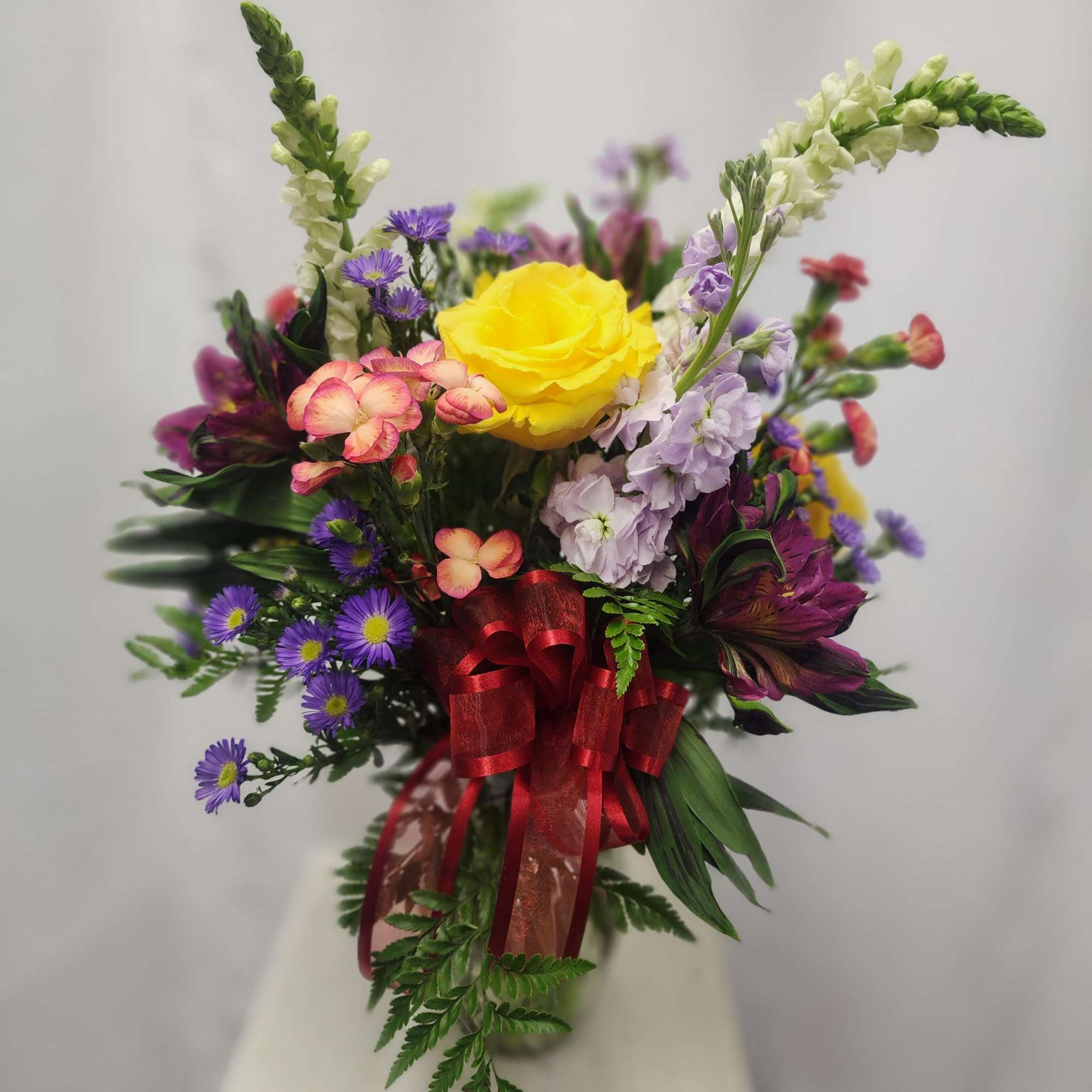 Colorful bouquet with a yellow rose and purple flowers tied with a red ribbon