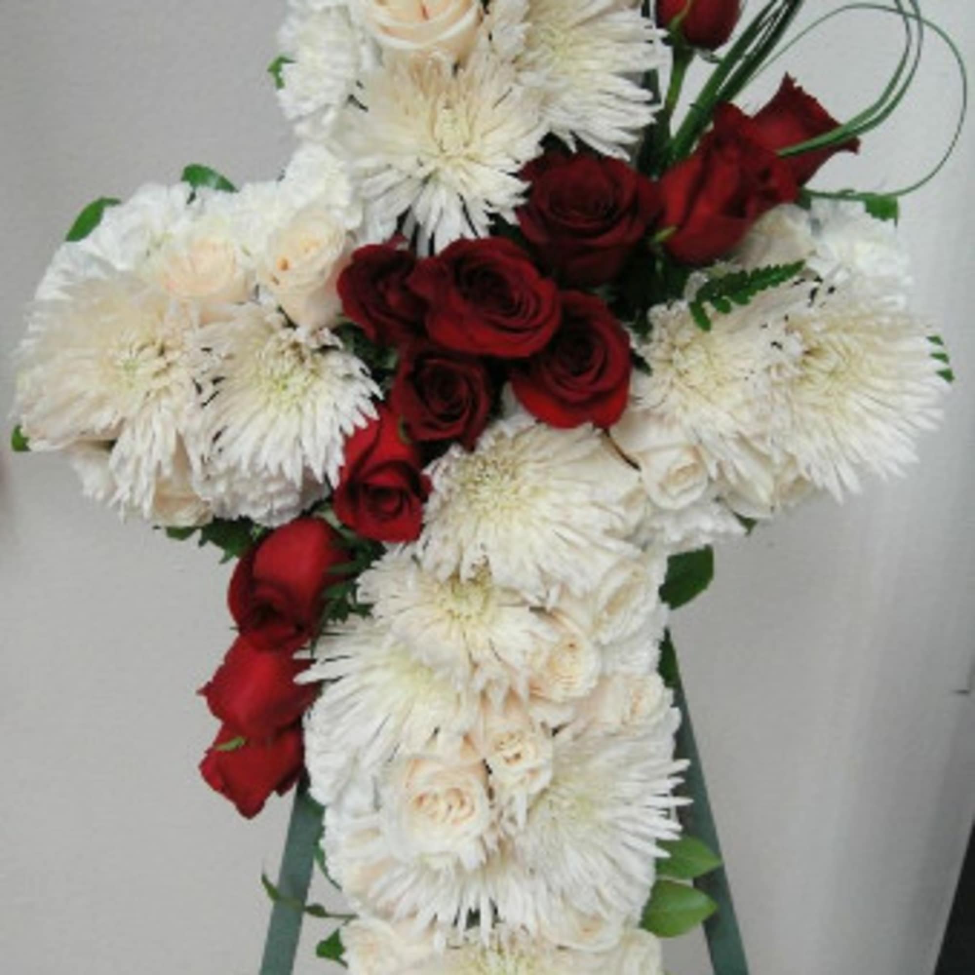 Standing floral cross with white flowers and red roses on an easel