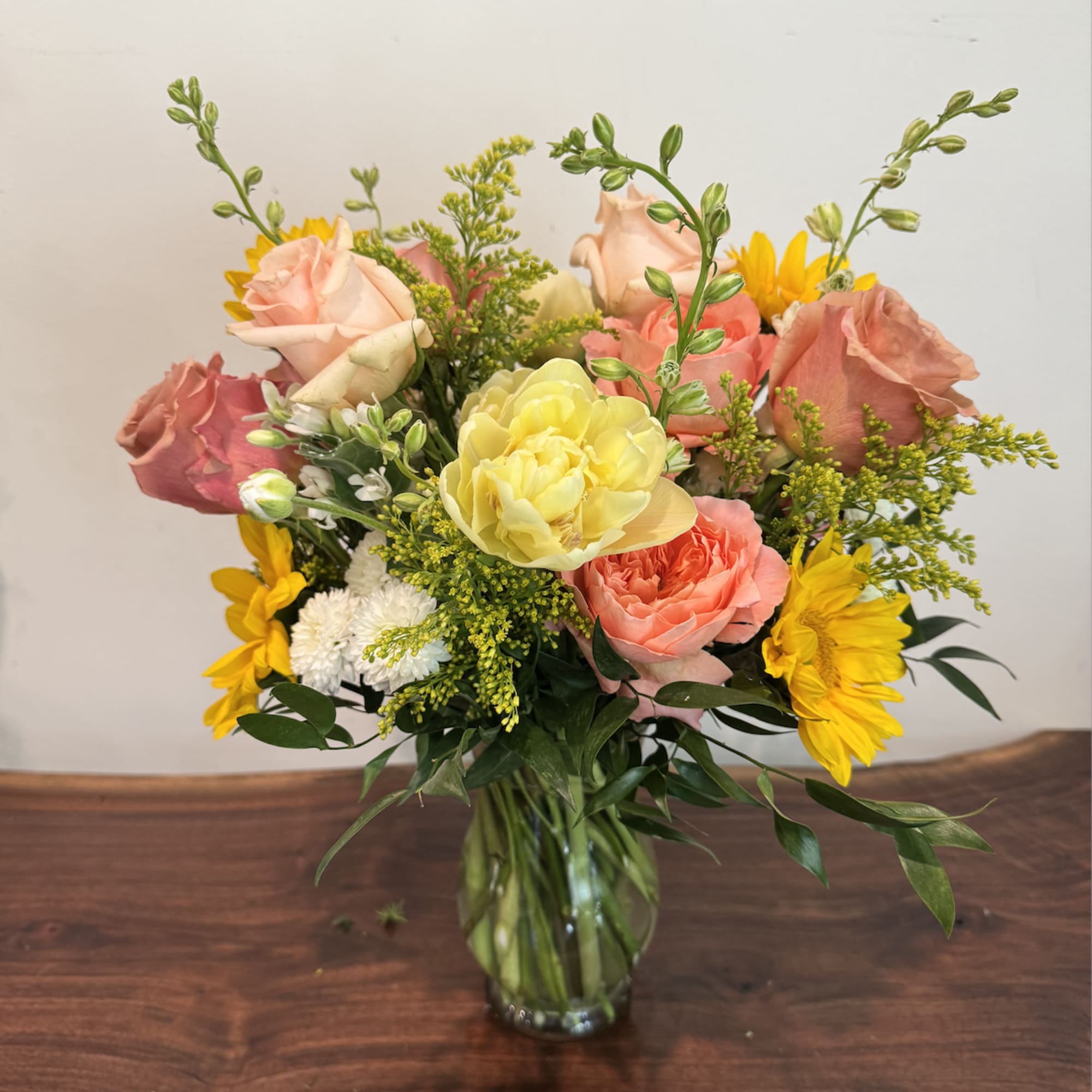 Peach and coral roses meet bold yellow sunflowers and seasonal stems in