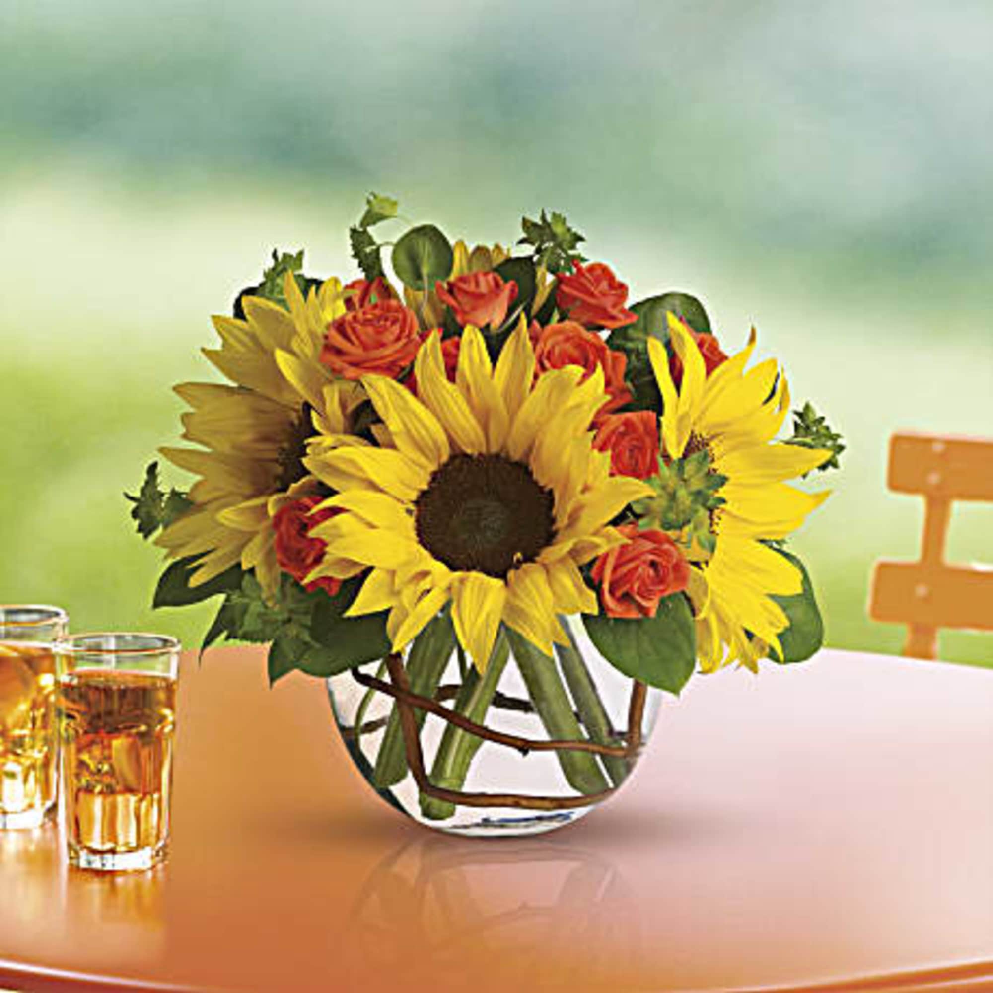 Sunflowers and orange roses arranged in a clear glass vase