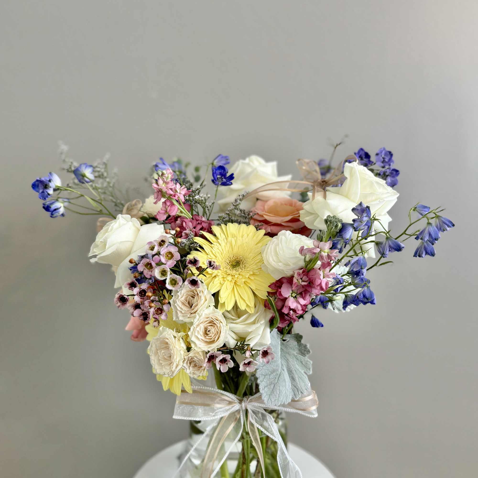 Mixed bouquet of pastel flowers in a glass vase with ribbon