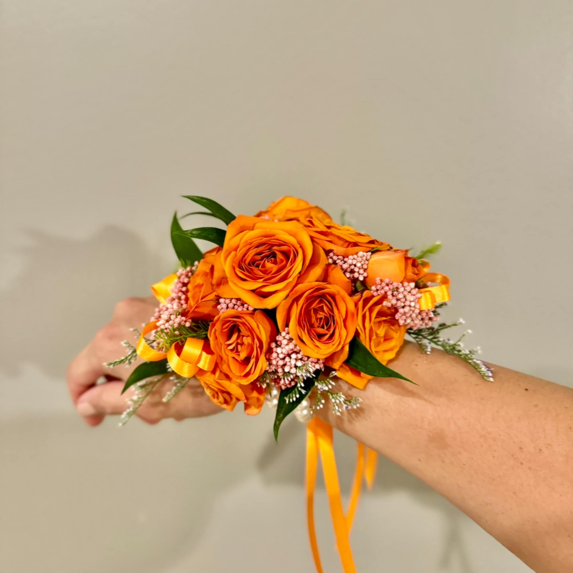 Orange rose wrist corsage with pink accents and ribbon