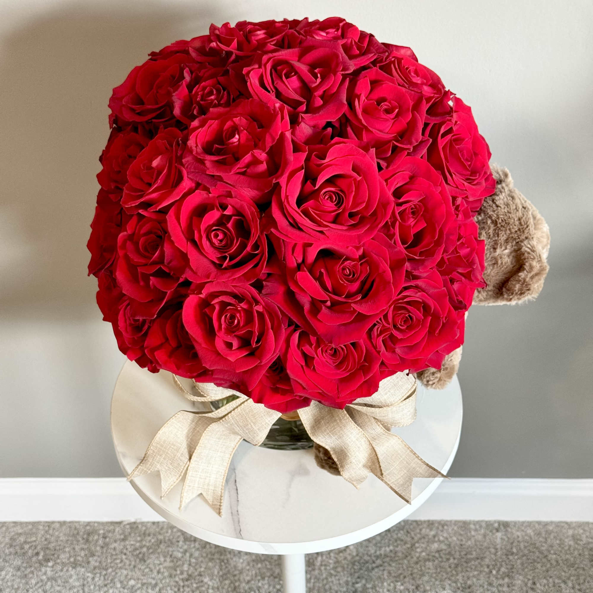 Round bouquet of red roses with a beige ribbon and teddy bear accents