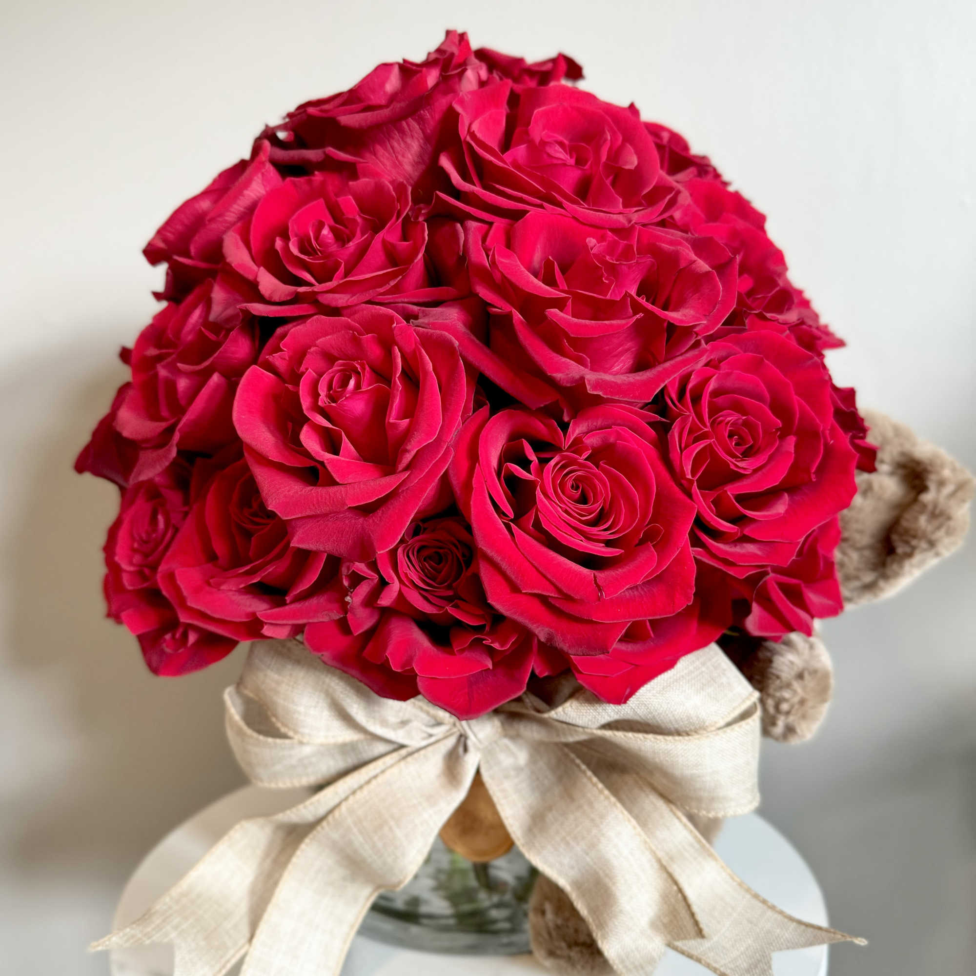 Bouquet of bright pink roses with a beige ribbon in a glass vase