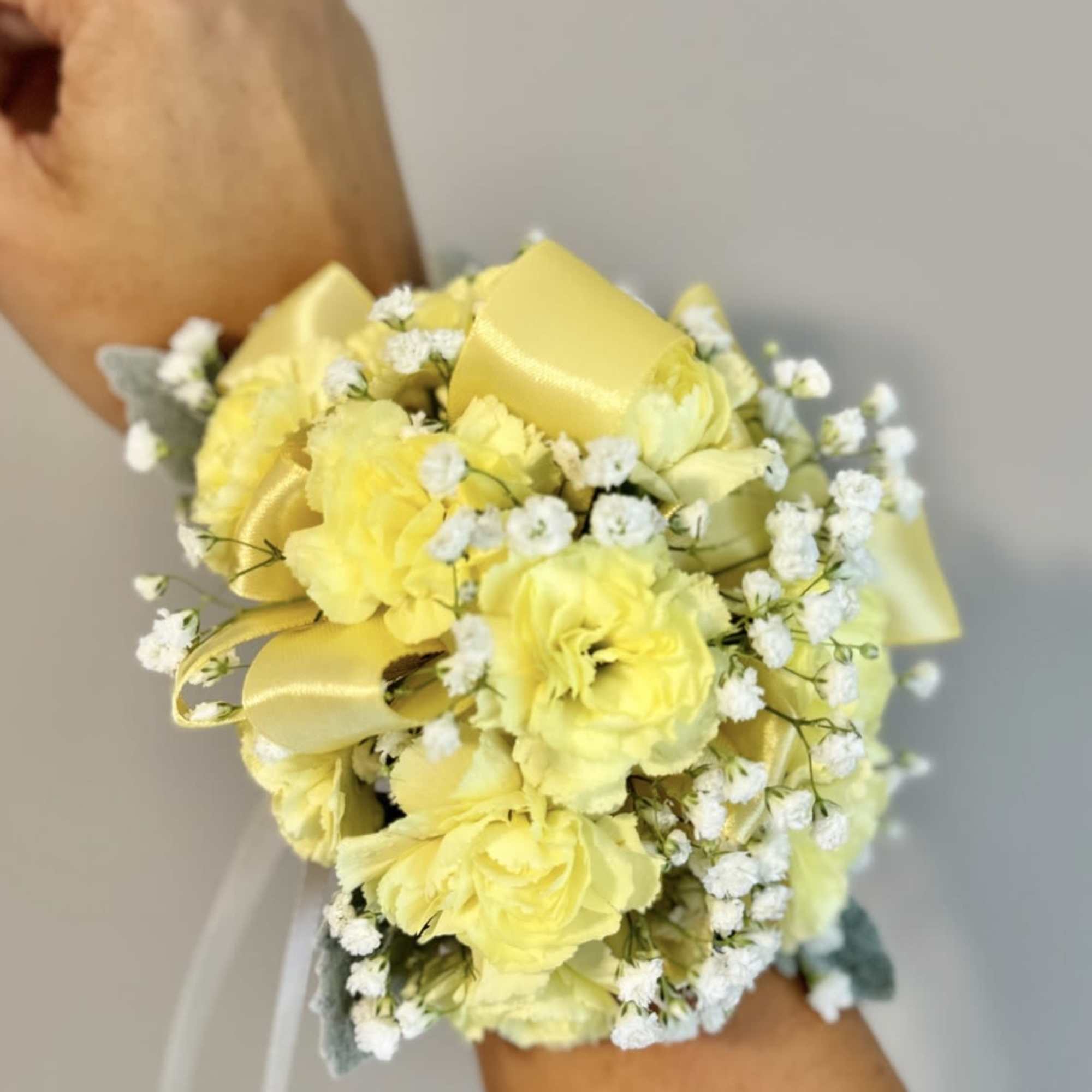 Yellow wrist corsage with small white filler flowers and satin ribbon