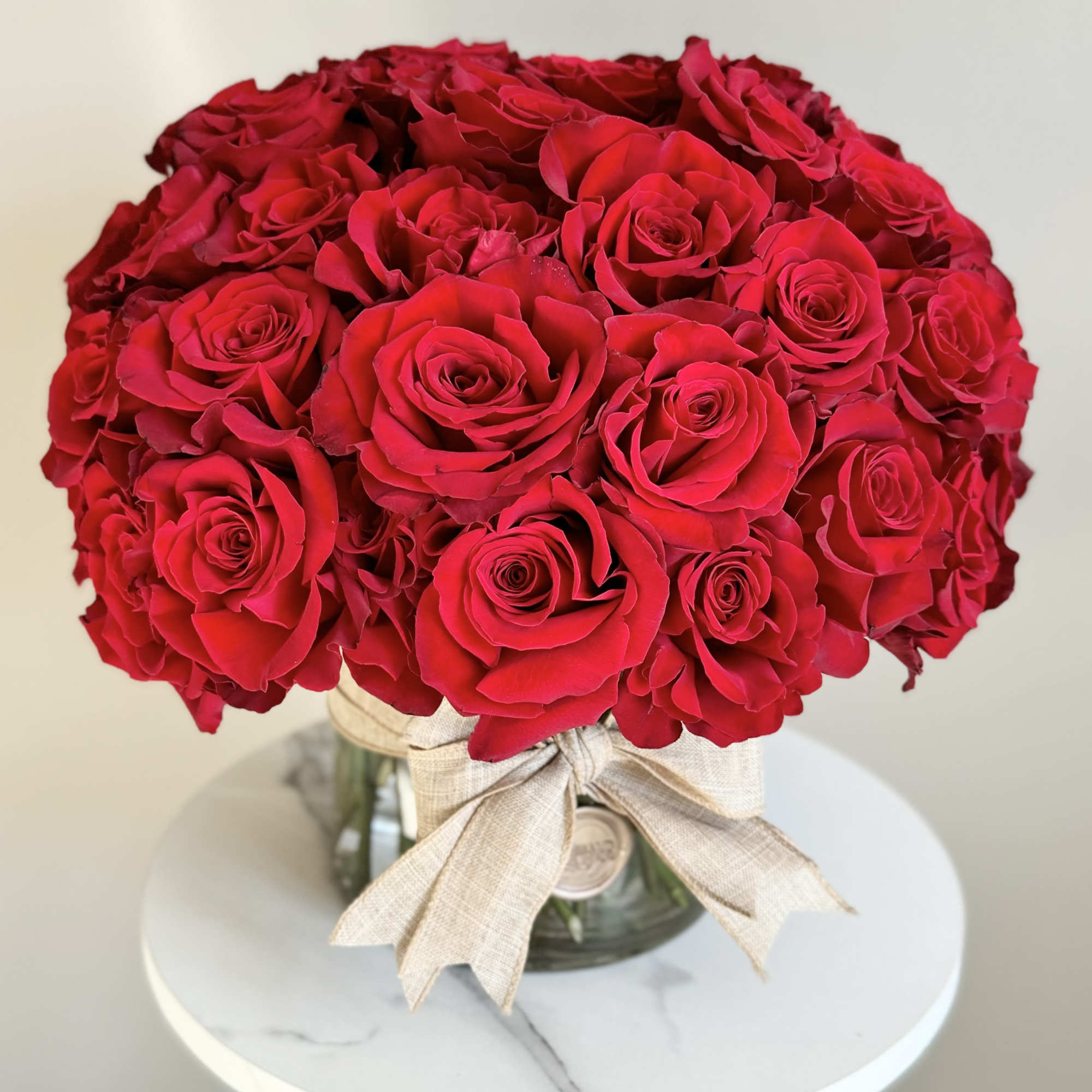 Bouquet of red roses in a glass vase with a beige ribbon