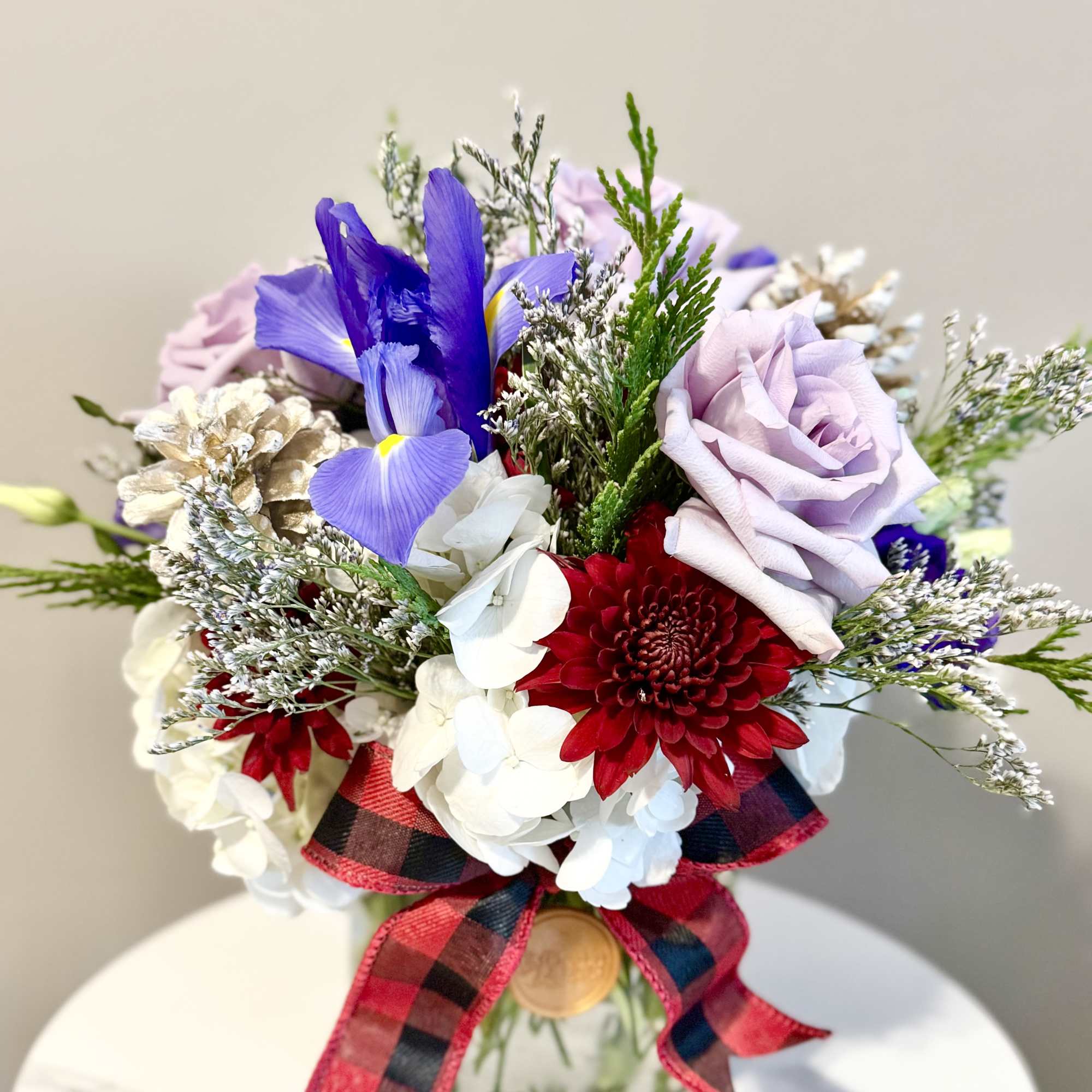 Bouquet of purple, red, and white flowers in a glass vase with a plaid ribbon