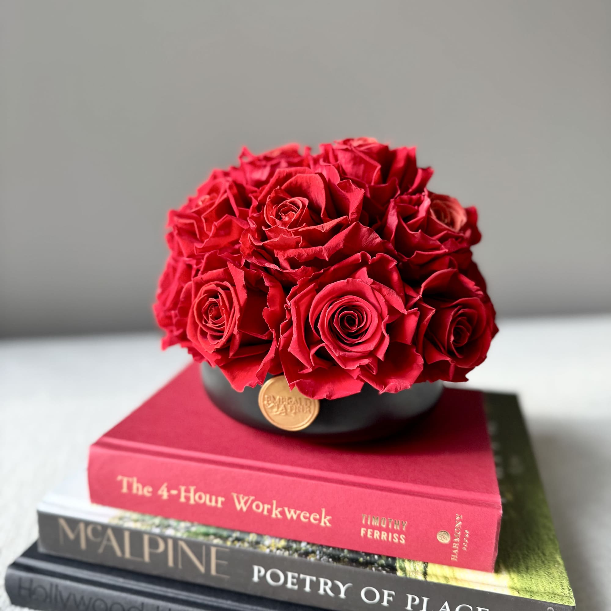 Red rose arrangement in a black round box on stacked books