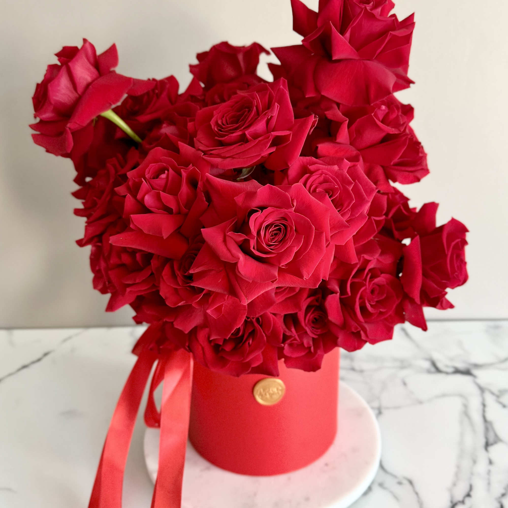 Red roses arranged in a round red box with ribbon