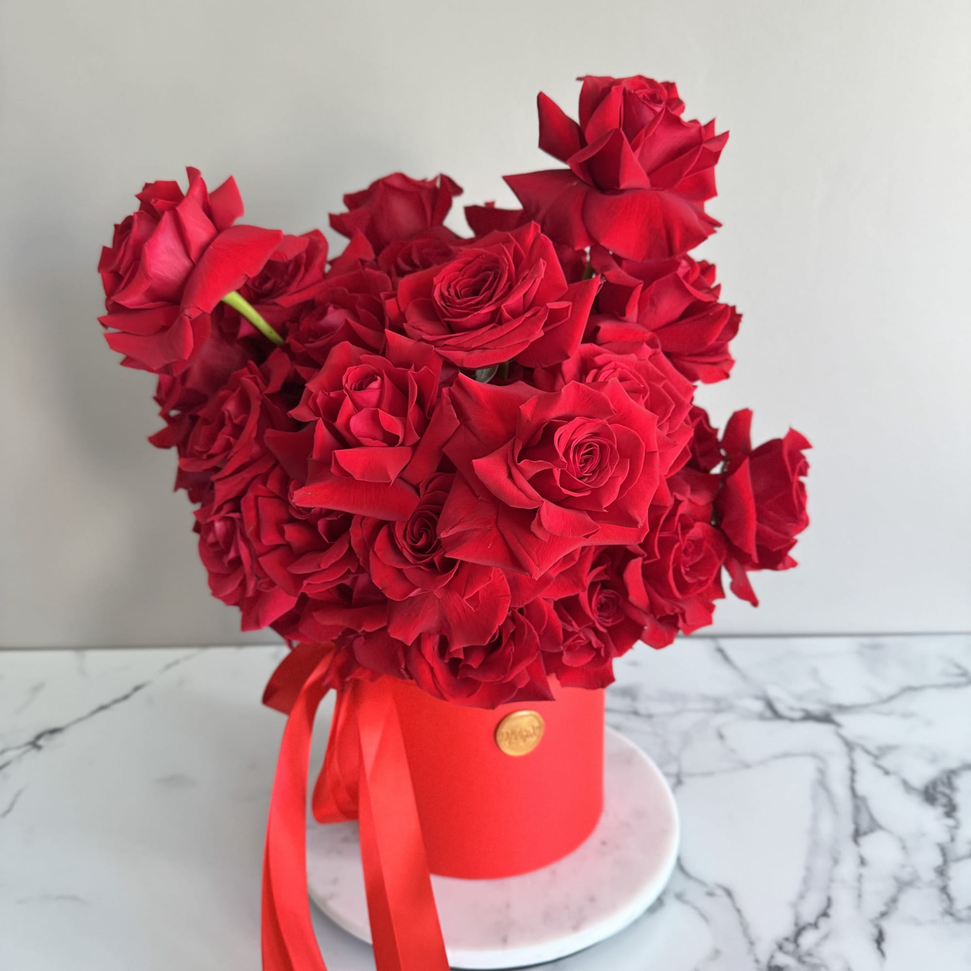 Red rose arrangement in a red hat box with a ribbon
