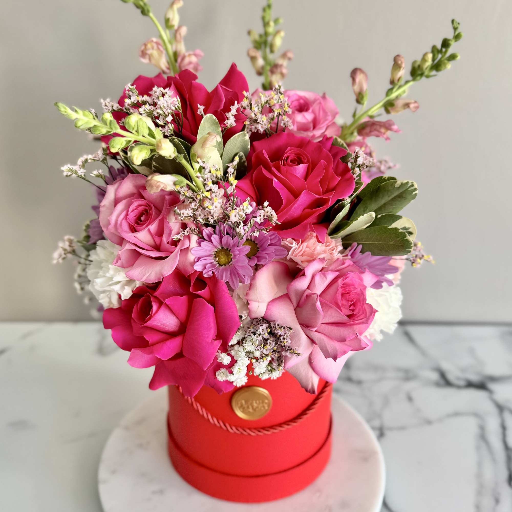 Pink and red rose bouquet in a red hat box on a round base