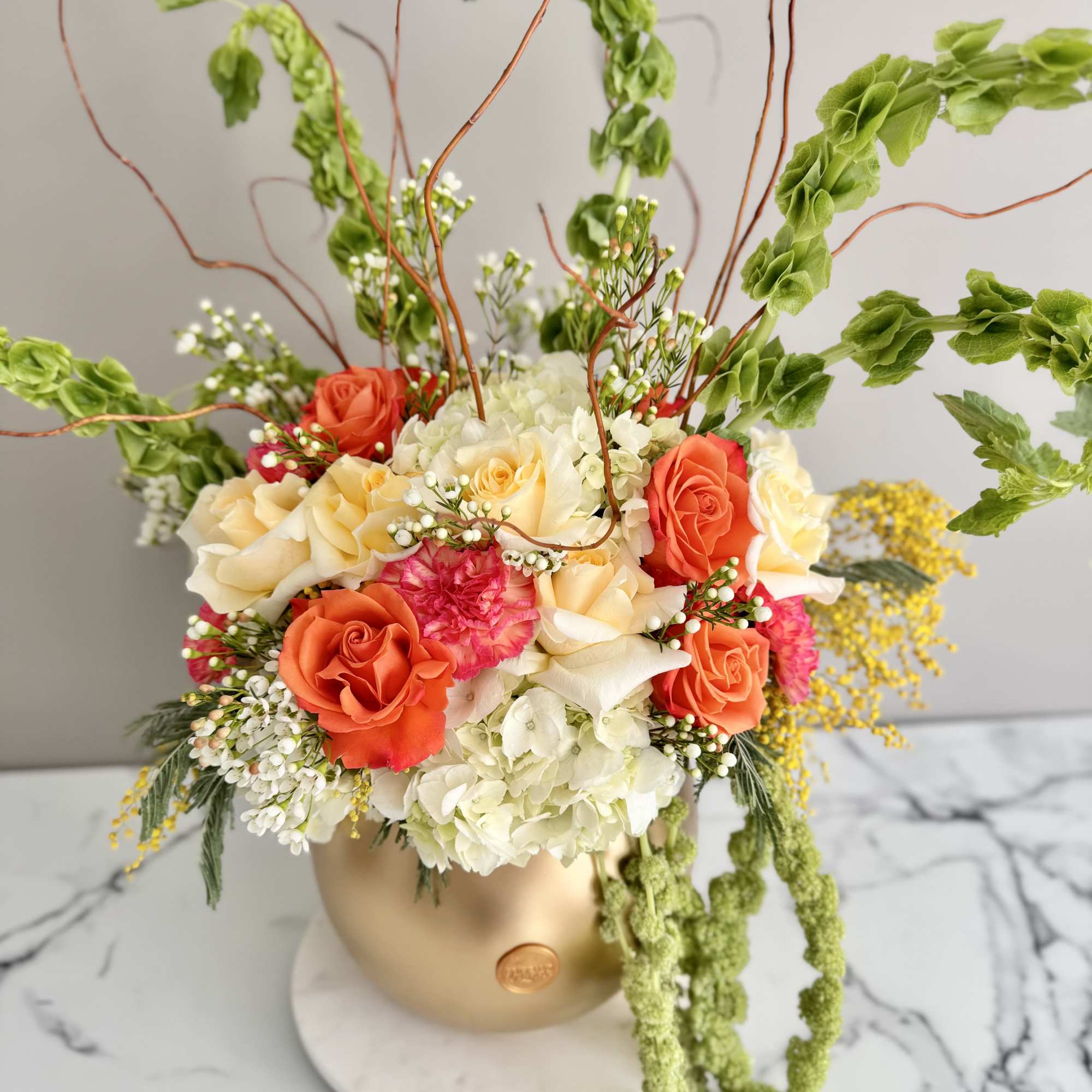 Mixed floral arrangement in a gold vase with orange and cream roses