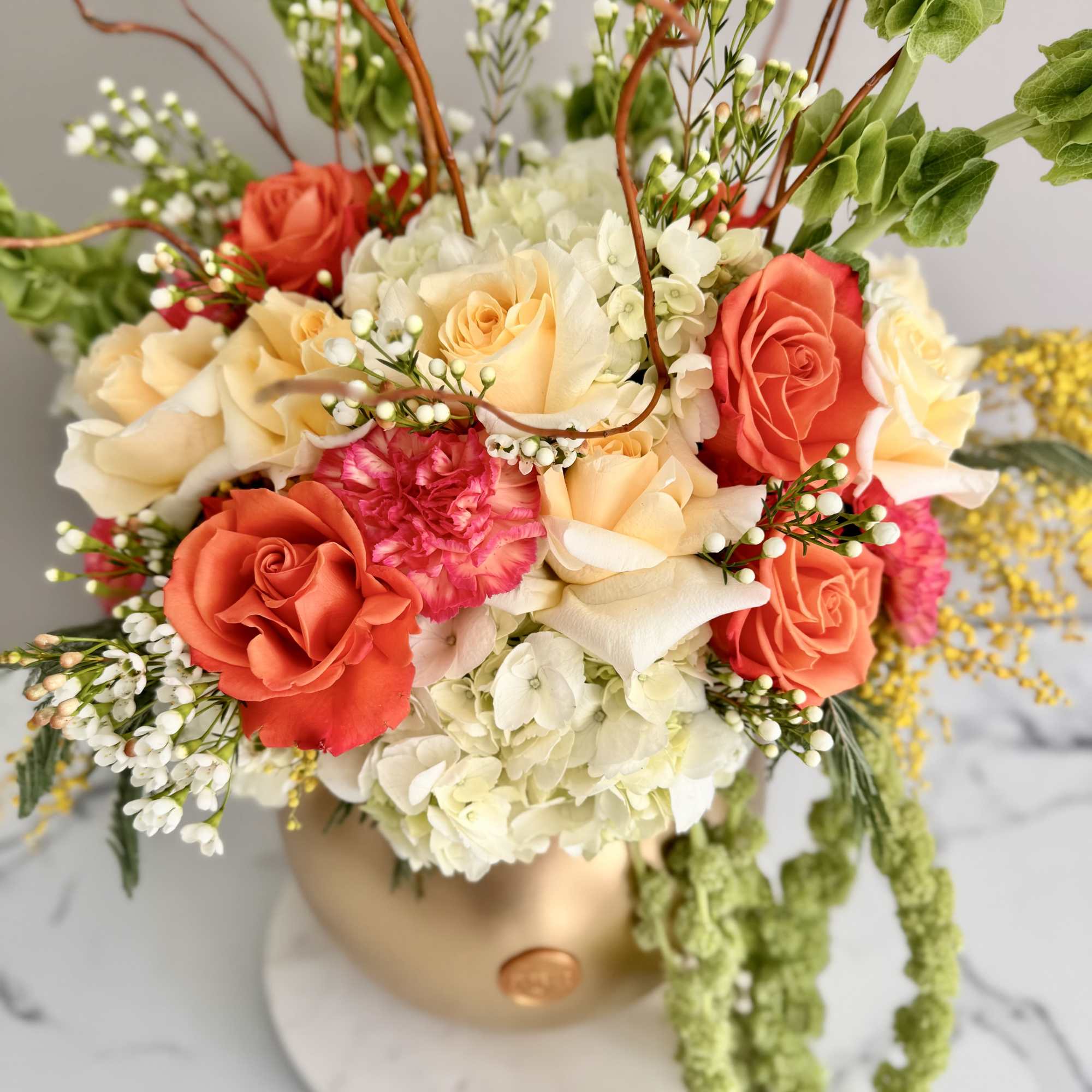 Coral and cream rose arrangement in a gold vase with trailing greenery