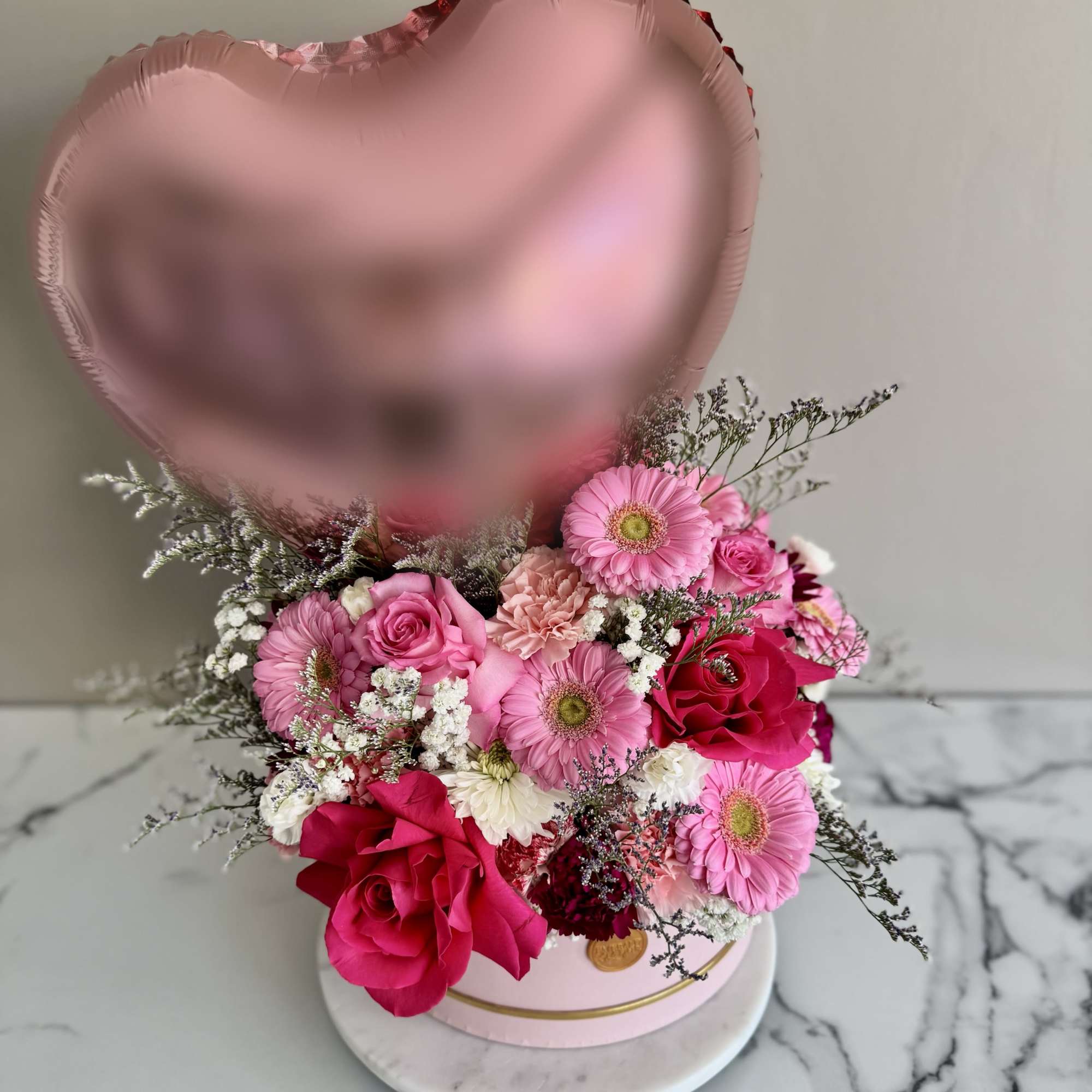 Pink heart balloon above a pink rose and gerbera bouquet in a round box