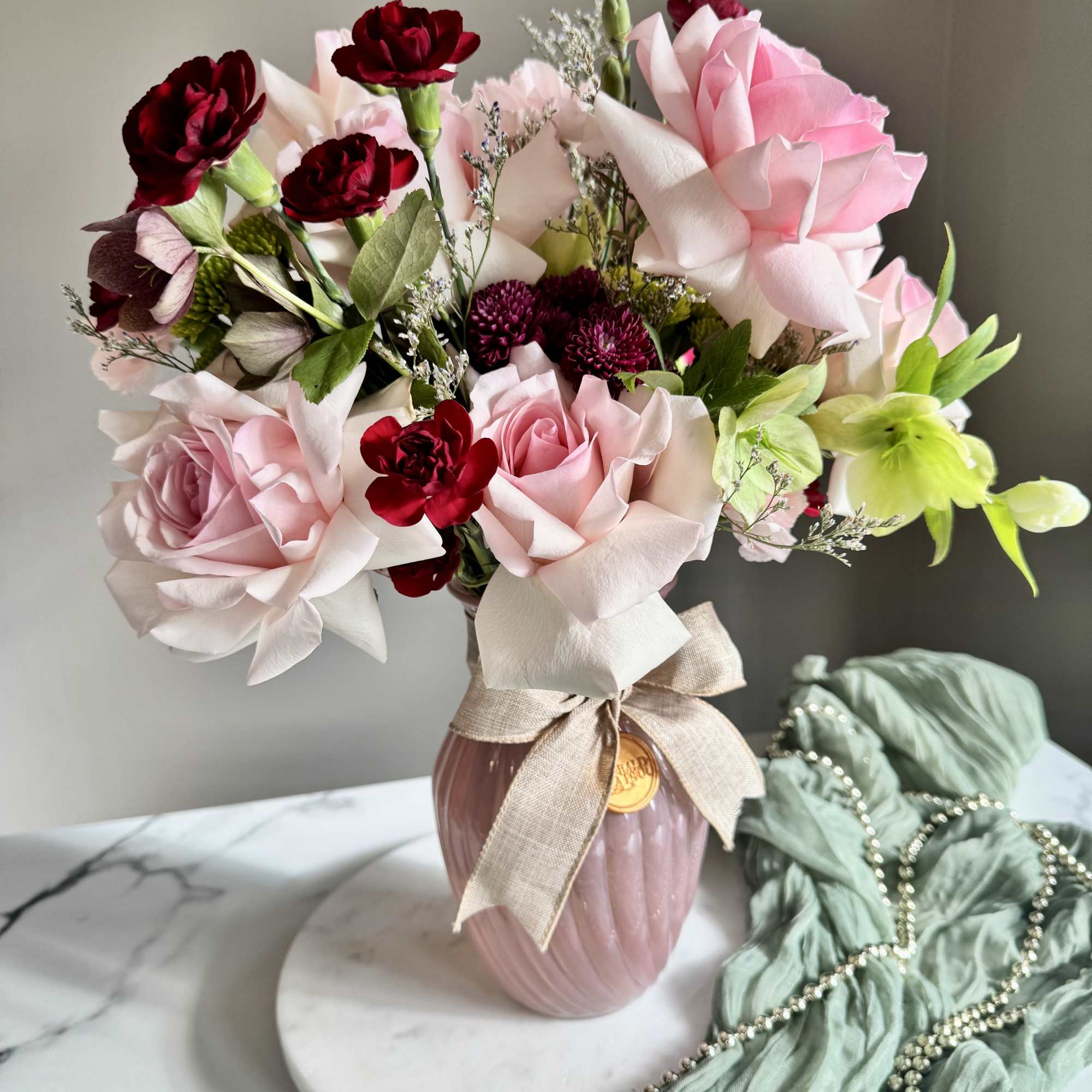 Pink and burgundy roses arranged in a vase with a ribbon bow