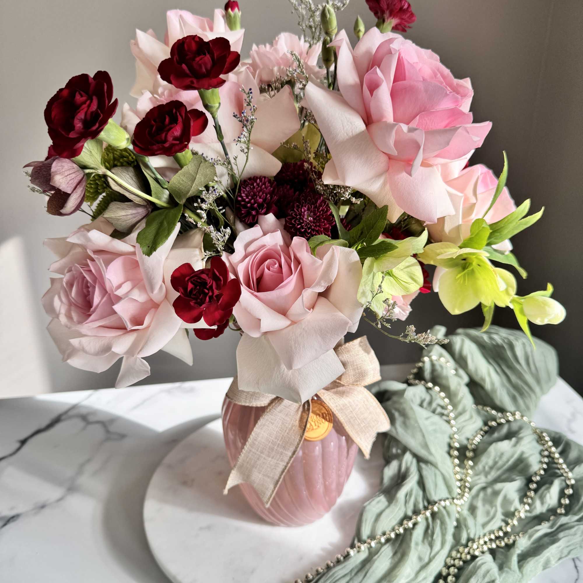 Pink and burgundy flower bouquet in a pink vase with a ribbon