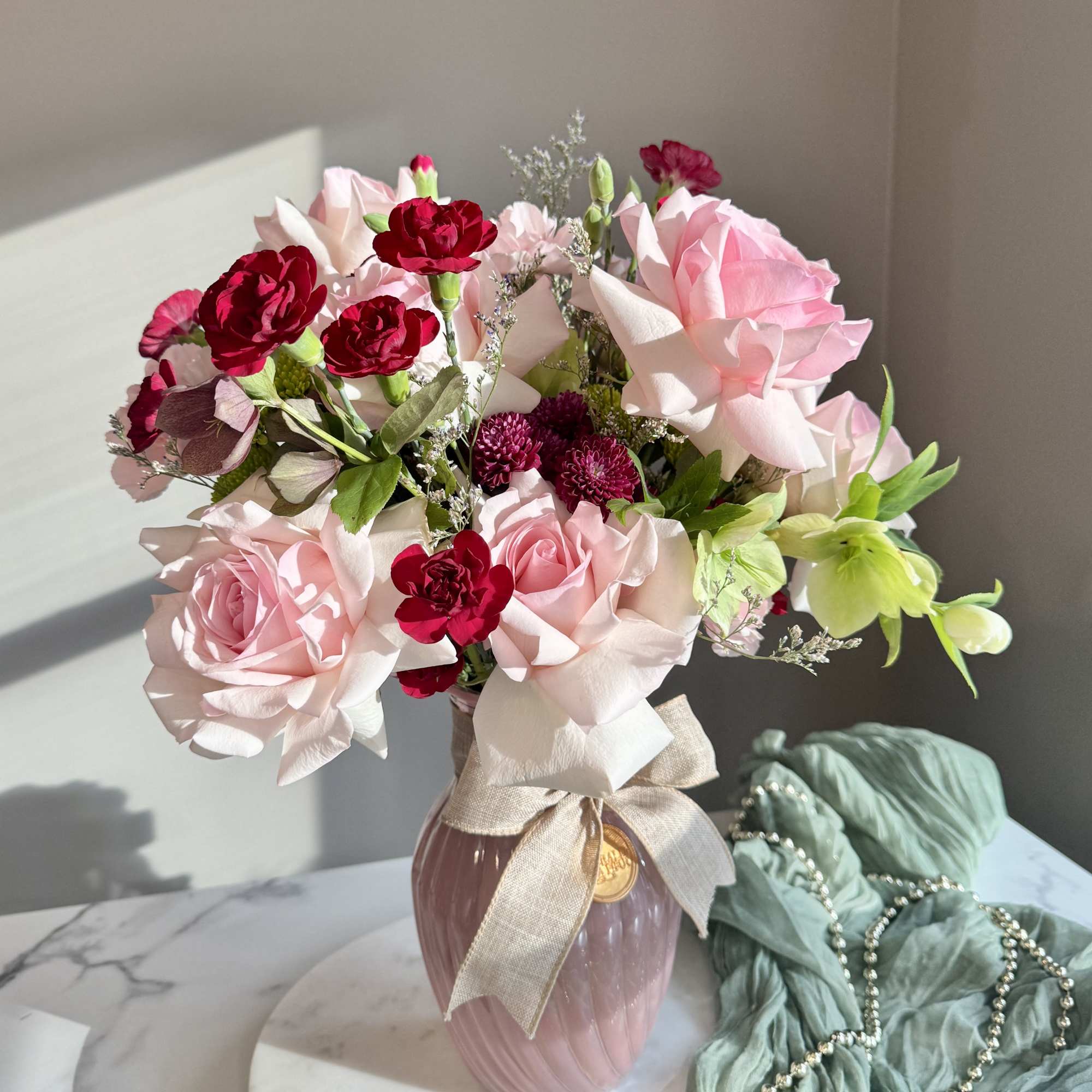 Pink and red flower bouquet in a ribbed pink vase with a ribbon