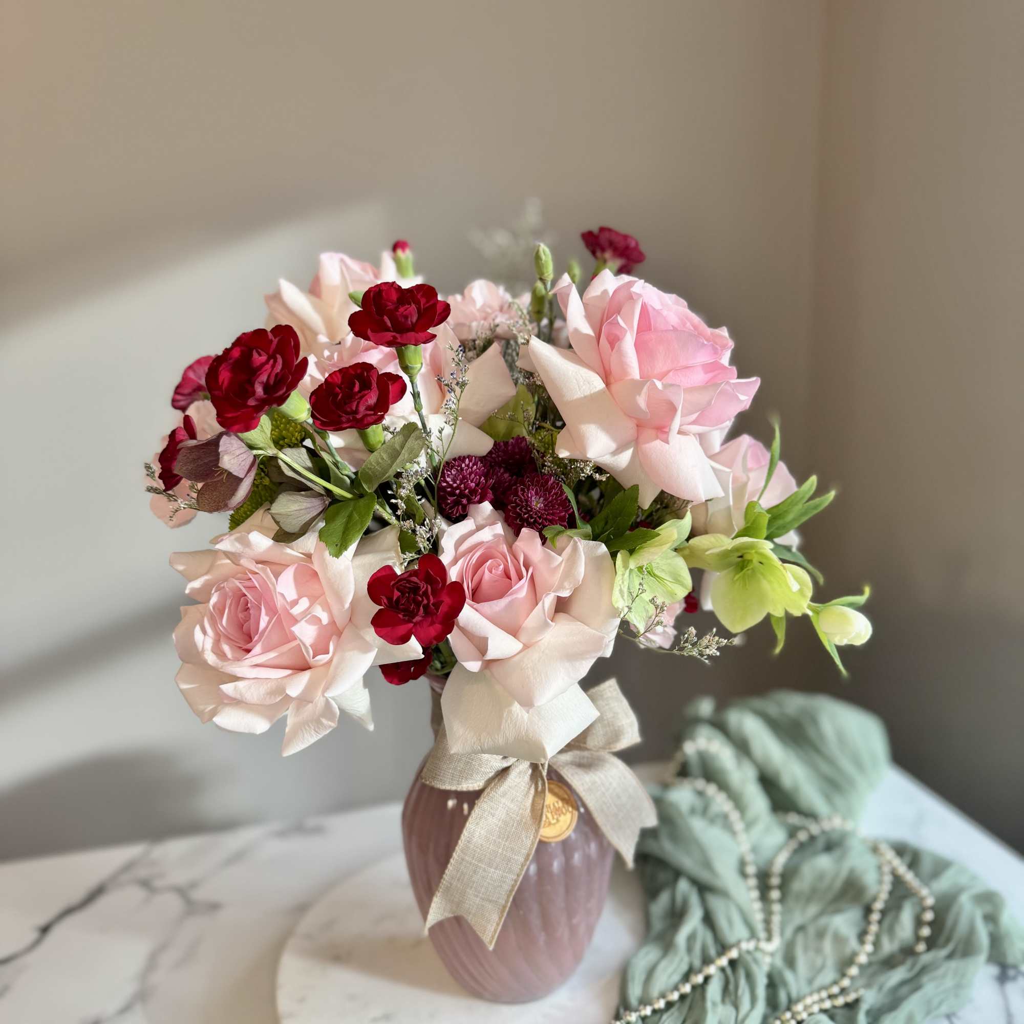 Pink and red rose bouquet in a mauve vase with a ribbon