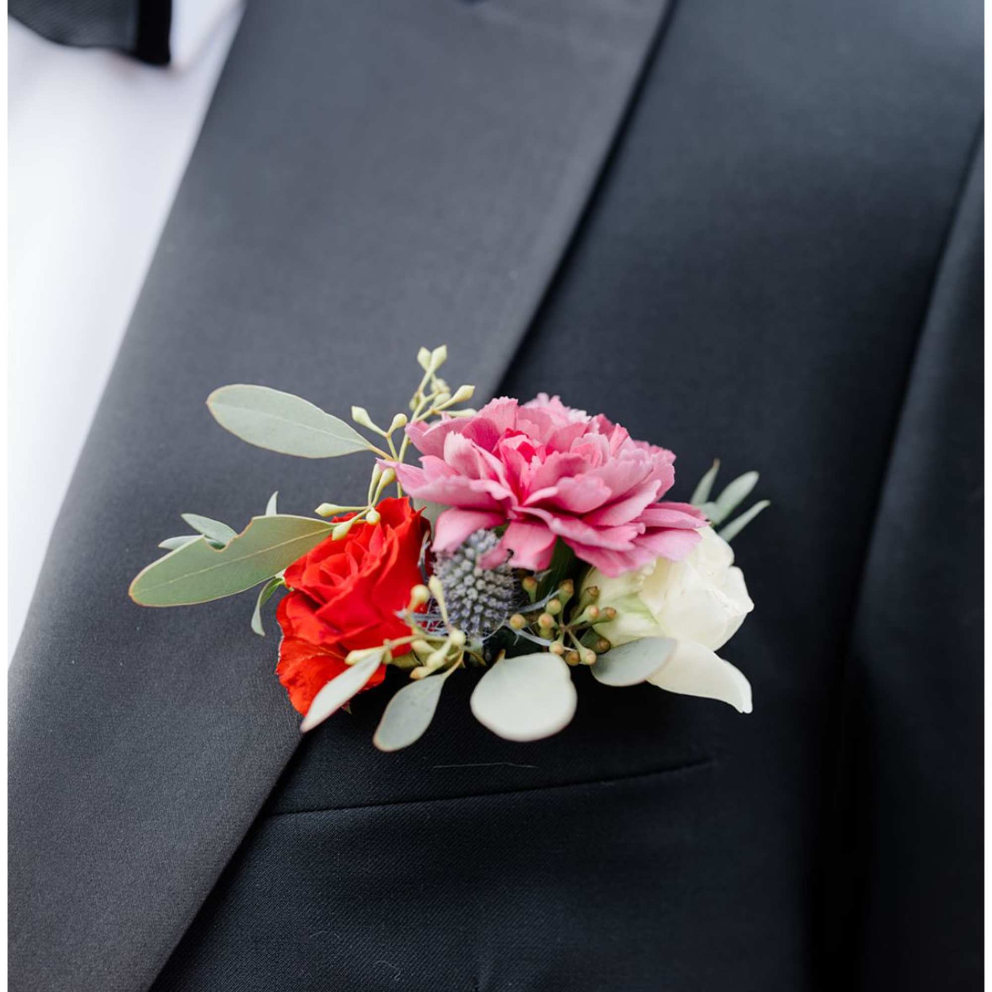 Boutonniere with pink, red, and white flowers on a black suit lapel