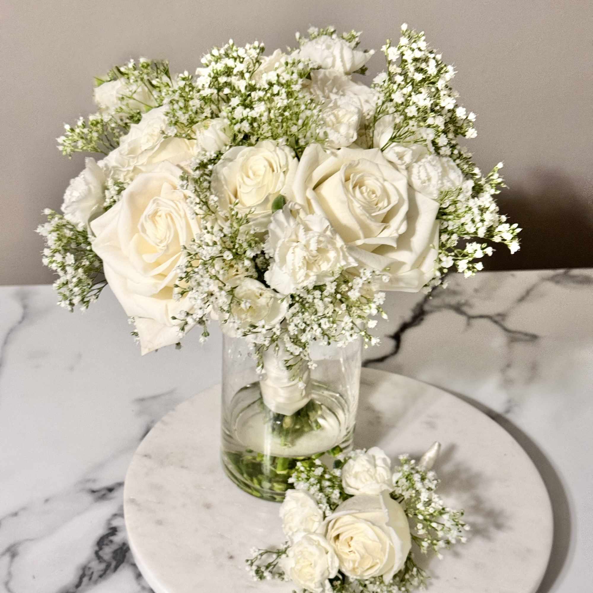 White rose bouquet in a clear glass vase with a matching boutonniere