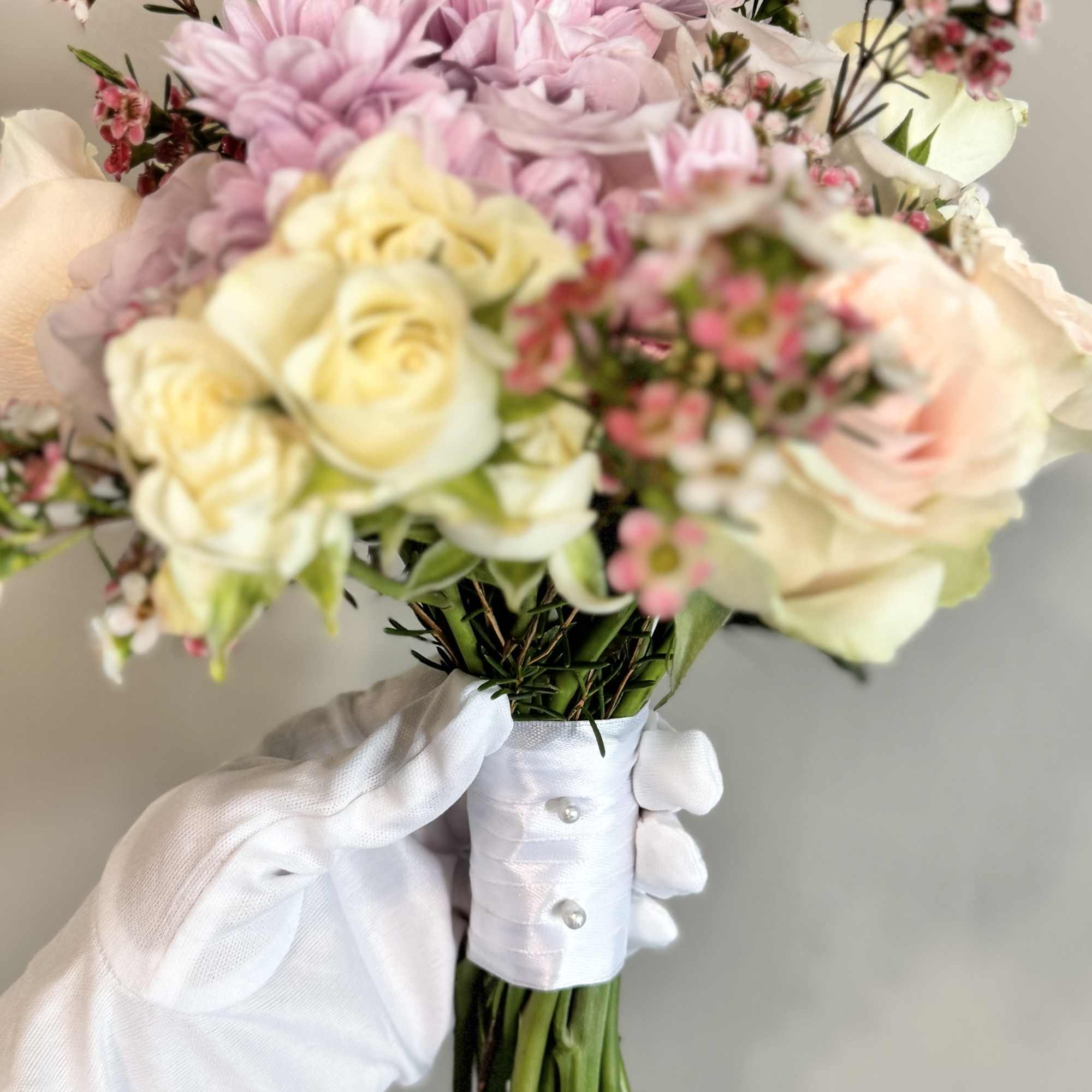 Handheld bouquet of pale pink and cream flowers wrapped in white ribbon